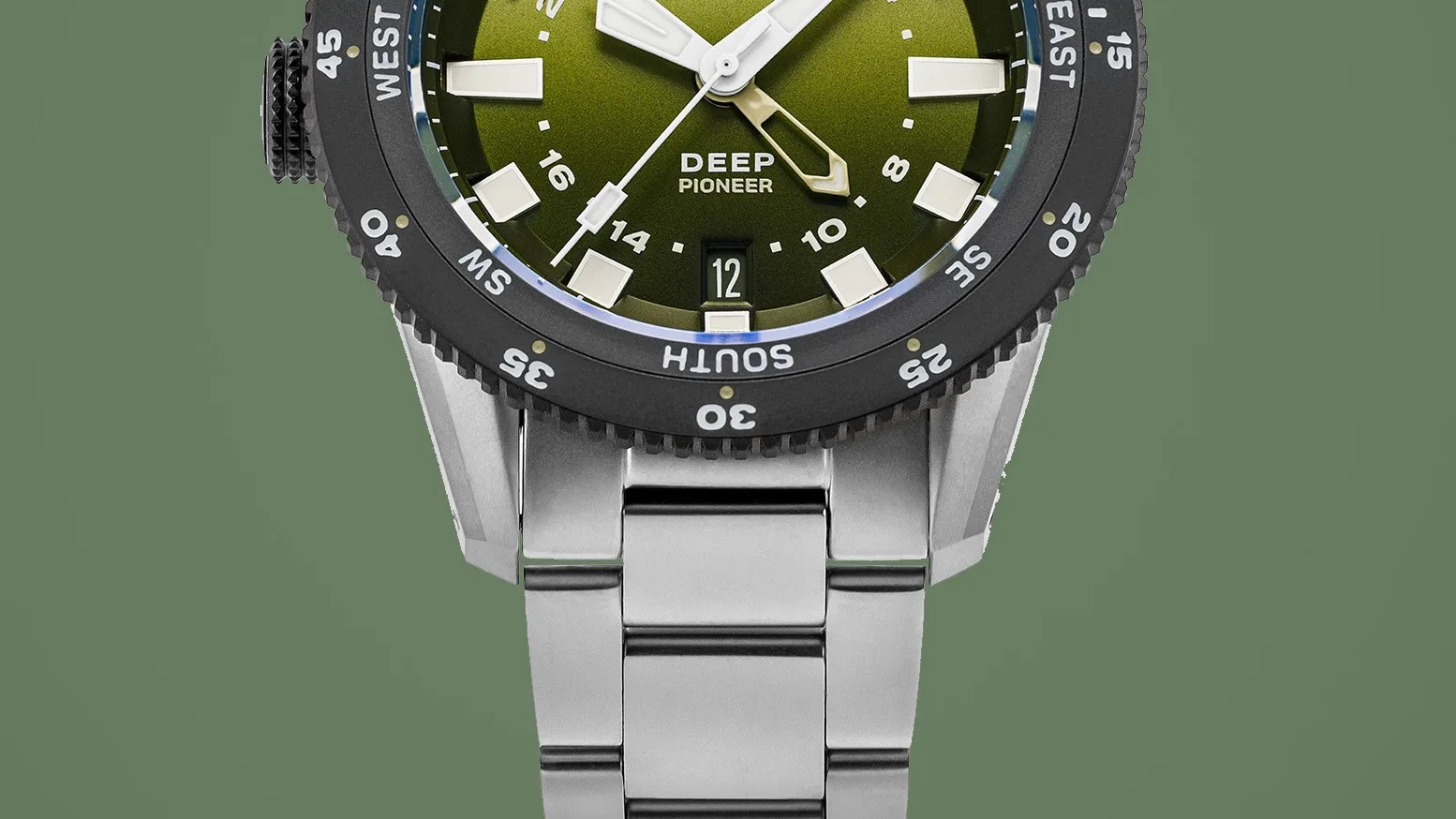 Close-up of a stainless steel watch with a green dial, white markers, and a black rotating bezel showing compass directions.