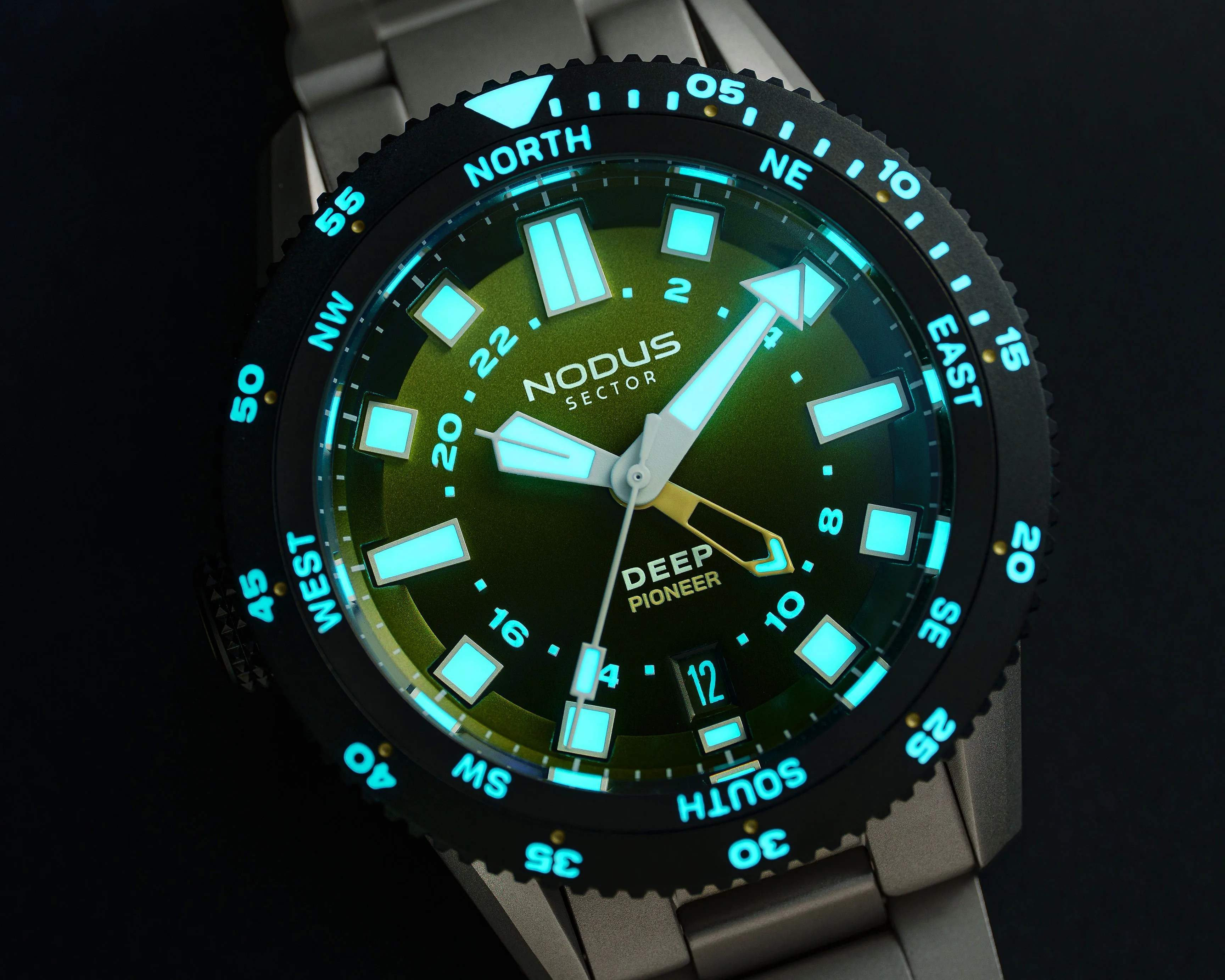 Close-up of a Nodus Sector Deep Pioneer watch with glowing blue hour markers and hands on a green dial with a metal bracelet.