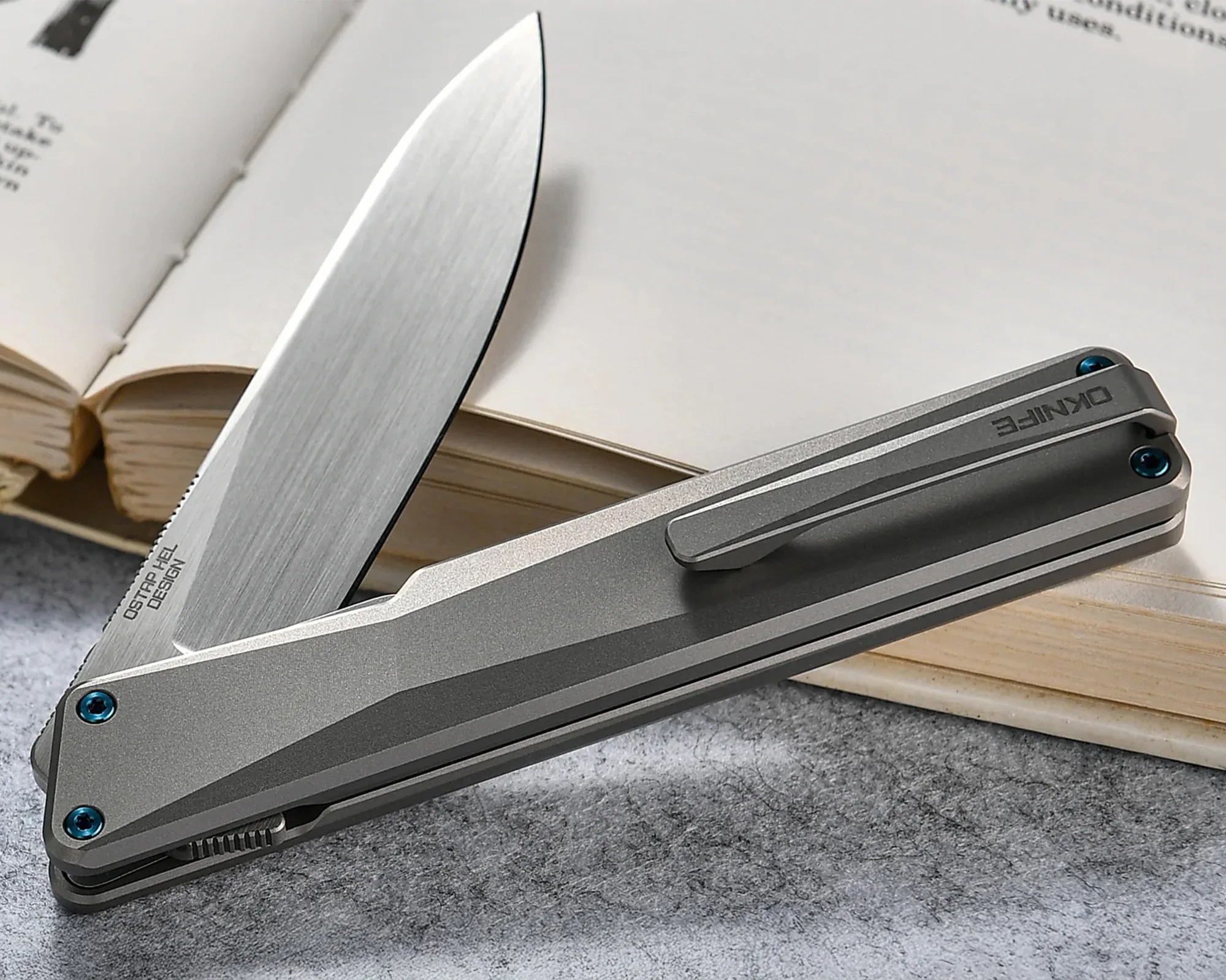 Gray folding pocket knife with partially open blade resting on an open book.