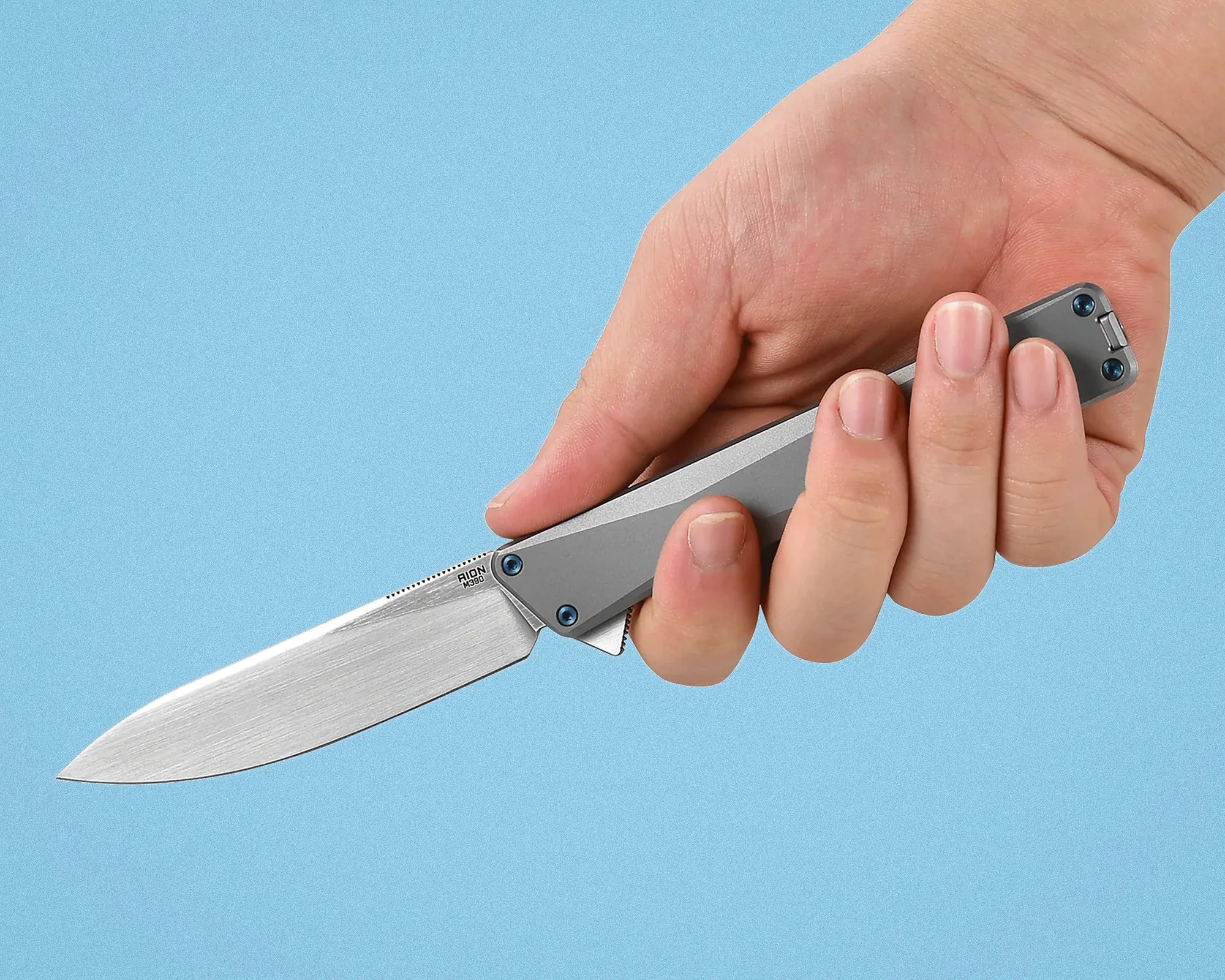 Hand holding a gray folding knife with a silver blade against a blue background.