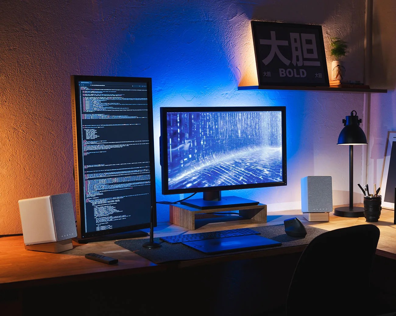 Desk setup with dual monitors, one vertical displaying code, the other horizontal showing a digital blue interface, with speakers, keyboard, mouse, and a lamp.
