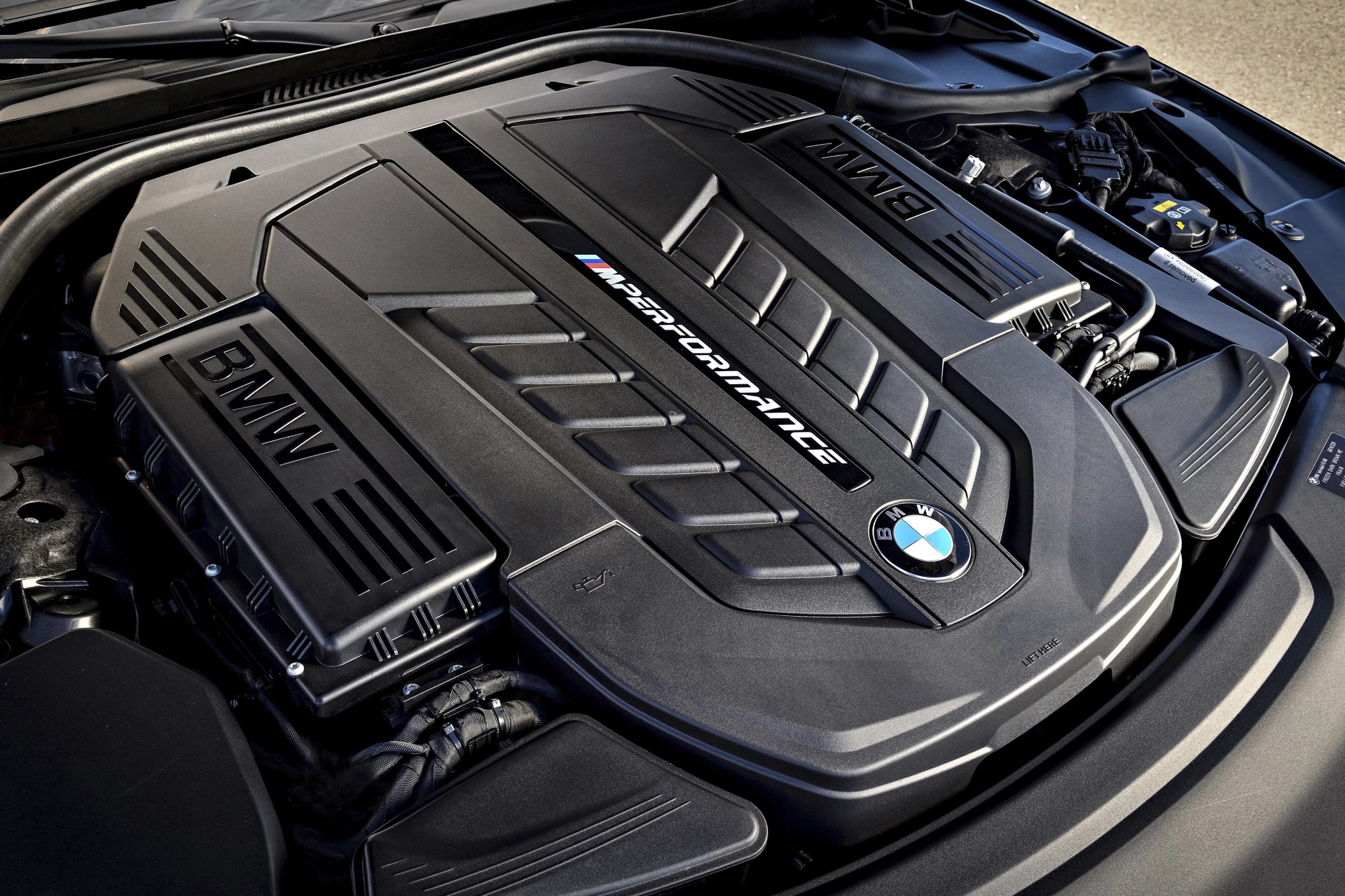 Black BMW engine cover with "M Performance" branding and BMW logo under an open car hood.