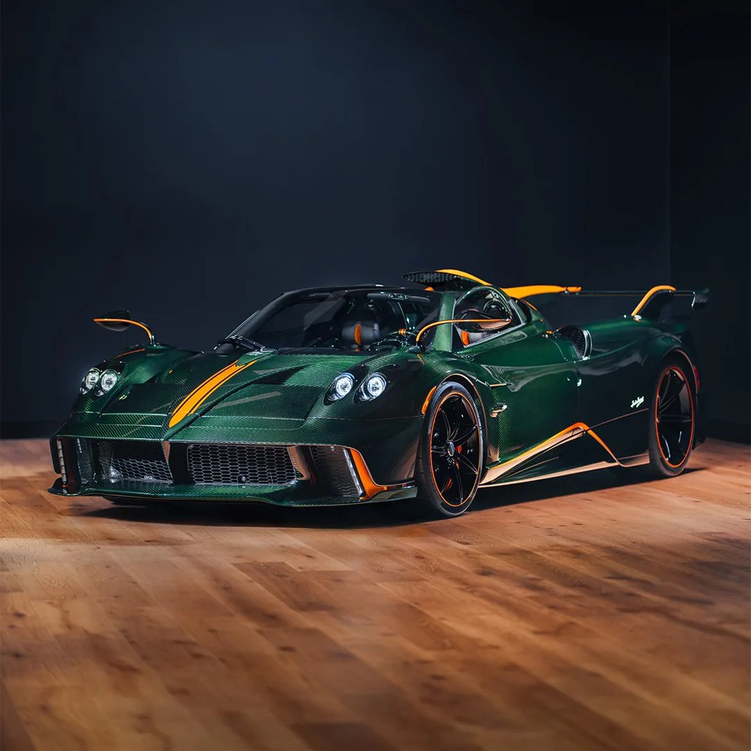 Dark green sports car with orange accents and black wheels on a wooden floor in a dark room.