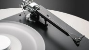Close-up of a black and silver tonearm on a modern turntable with a frosted vinyl record.