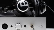 Black Pro-Ject Audio Systems headphones resting on a silver audio amplifier with input selector and cable connections.