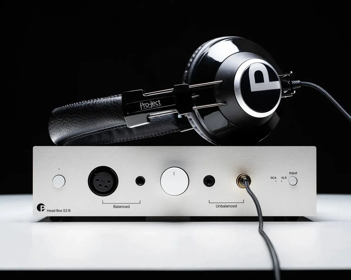 Silver Pro-Ject Head Box S3 B headphone amplifier with black Pro-Ject headphones resting on top.