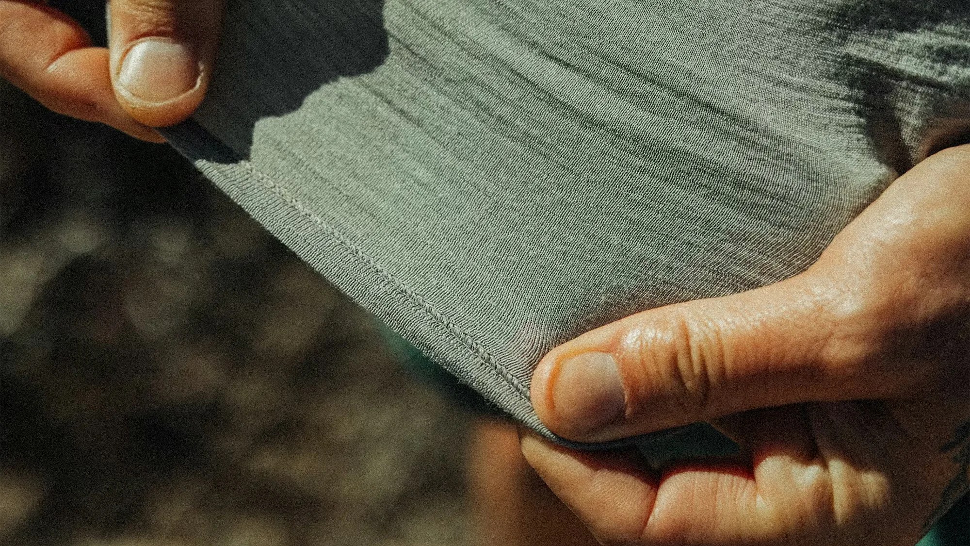 Close-up of hands holding and stretching the hem of a light gray ribbed fabric garment.