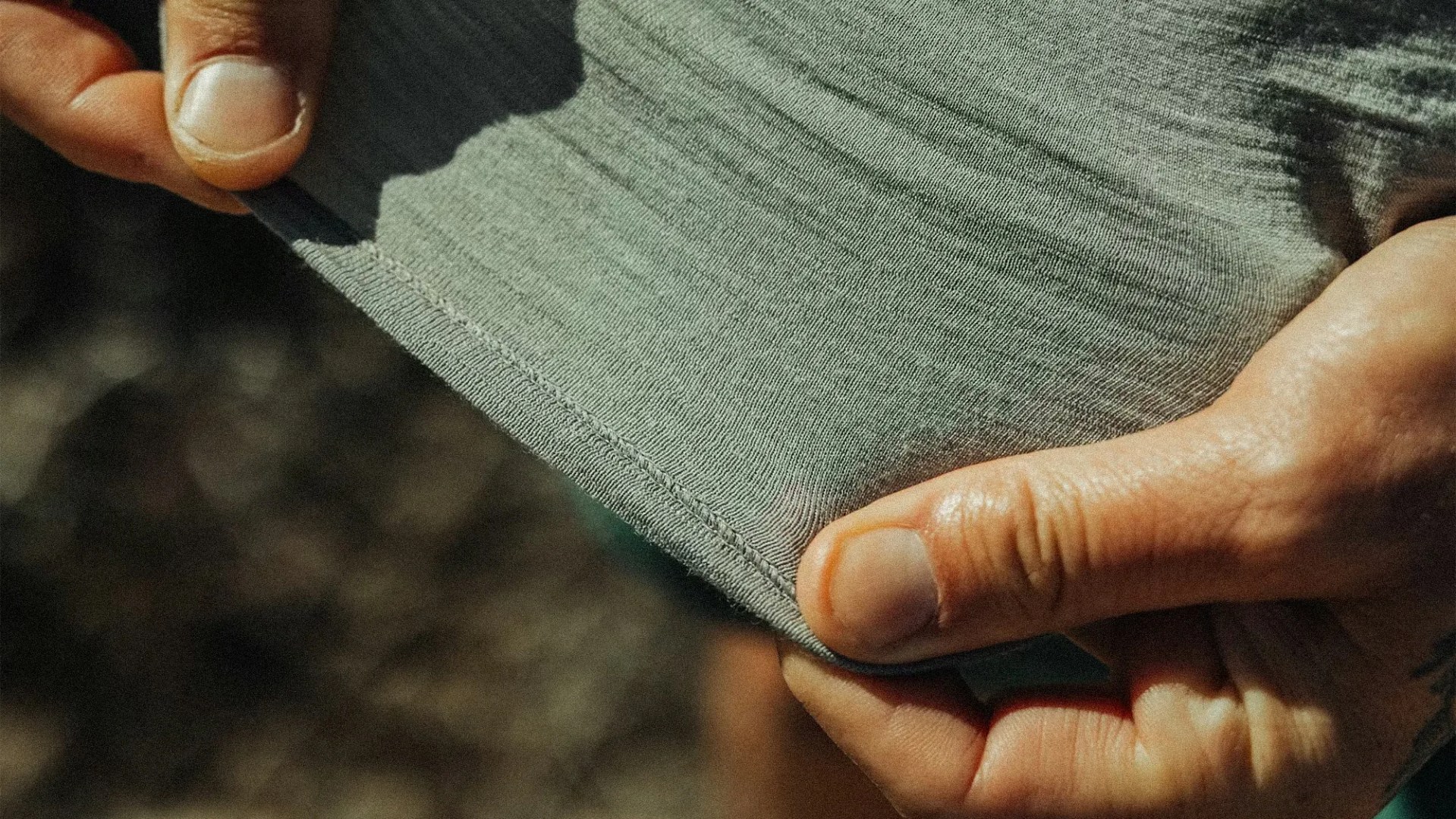 Close-up of hands holding and stretching the hem of a light gray ribbed fabric garment.