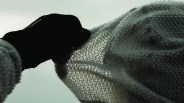 Person wearing a black glove holding up a loosely knit, light-colored fabric against a pale sky.