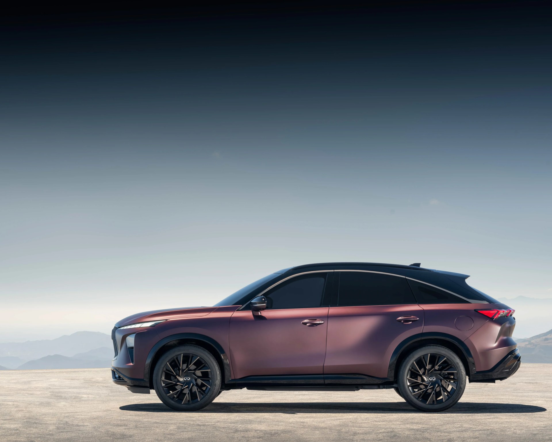 Side view of a matte purple Infiniti SUV with black roof and wheels on a flat surface with mountains in the background.