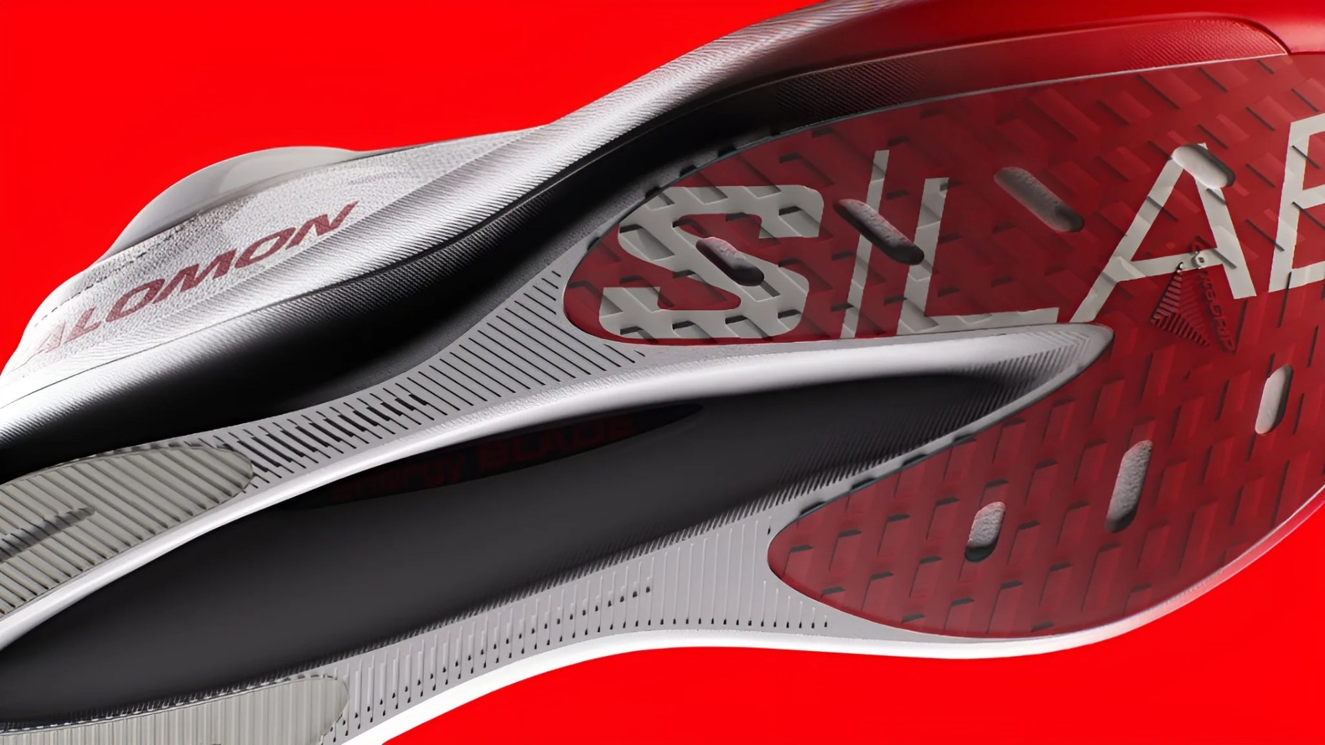 Close-up of the sole of a white and red Salomon shoe with textured grip against a red background.
