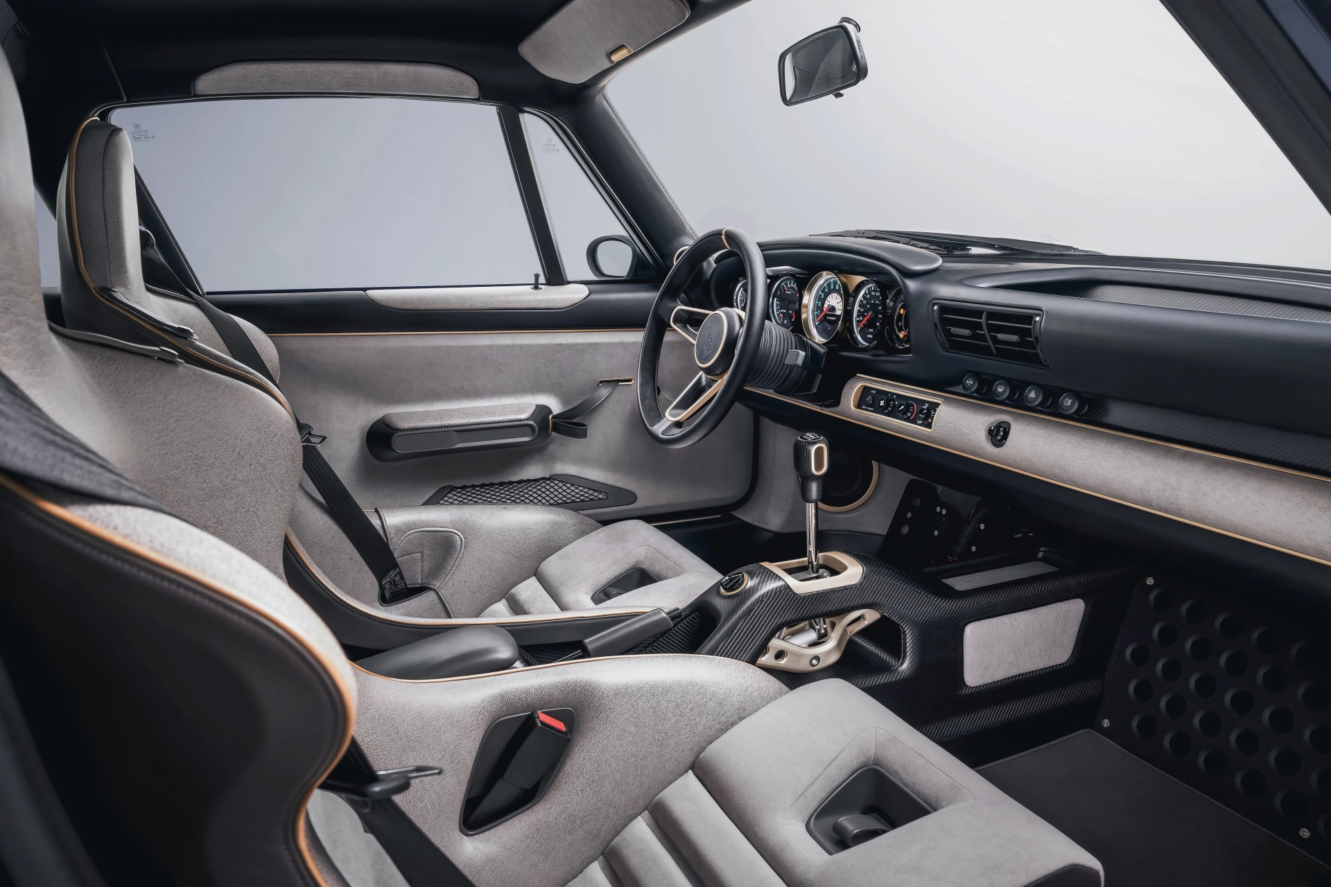 Car interior with light gray suede seats, black steering wheel, carbon fiber center console, and beige dashboard accents.