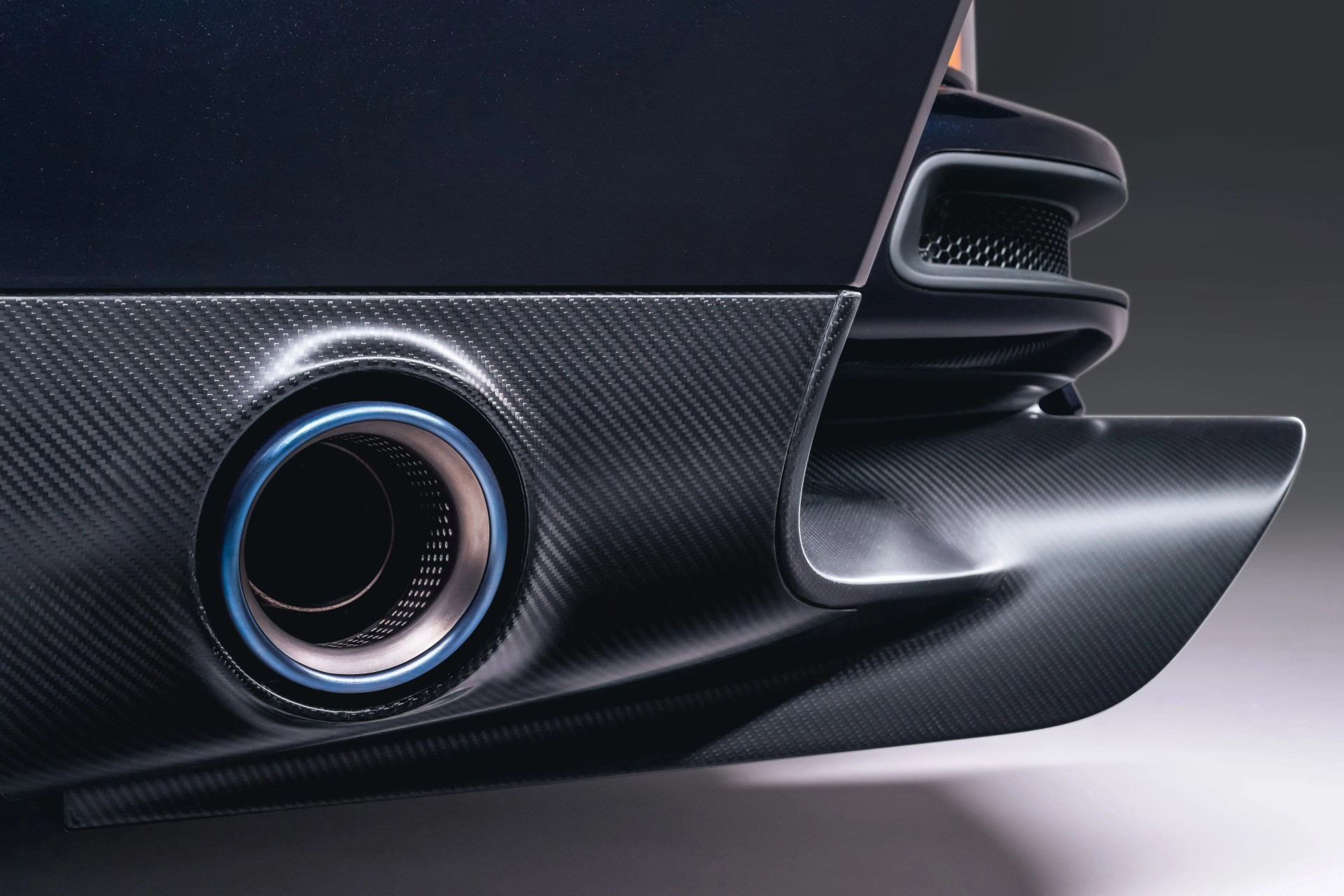 Close-up of a car's rear carbon fiber diffuser with a blue-tinted exhaust pipe.