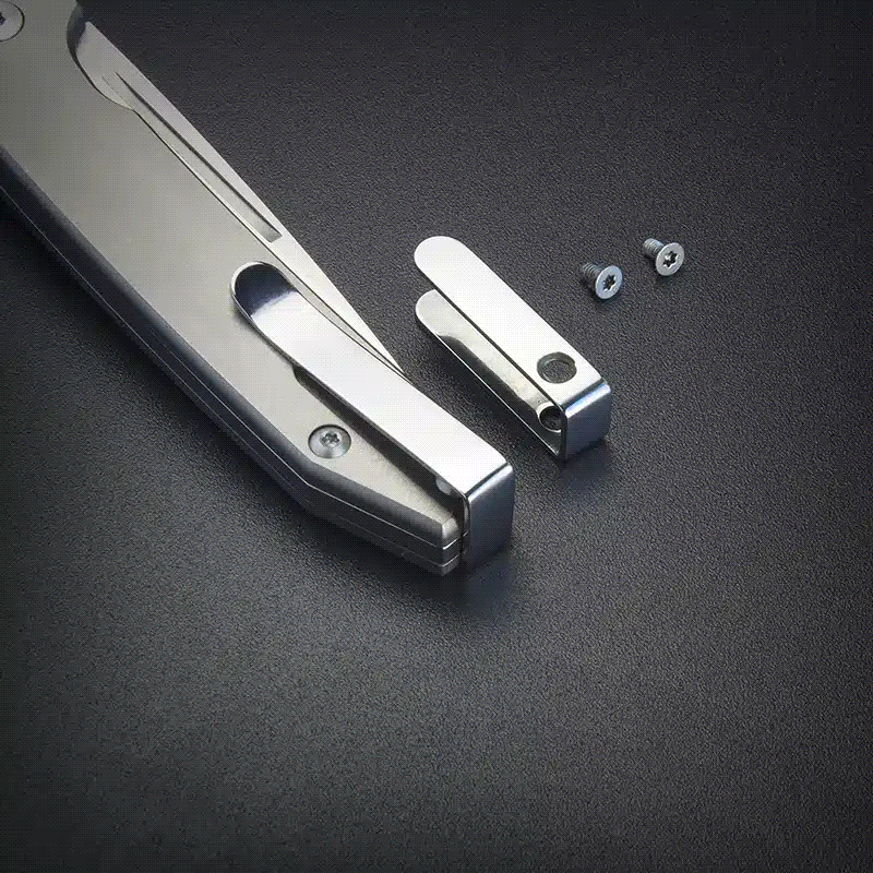 Silver metal folding knife with a detachable clip and two small screws on a dark textured surface.