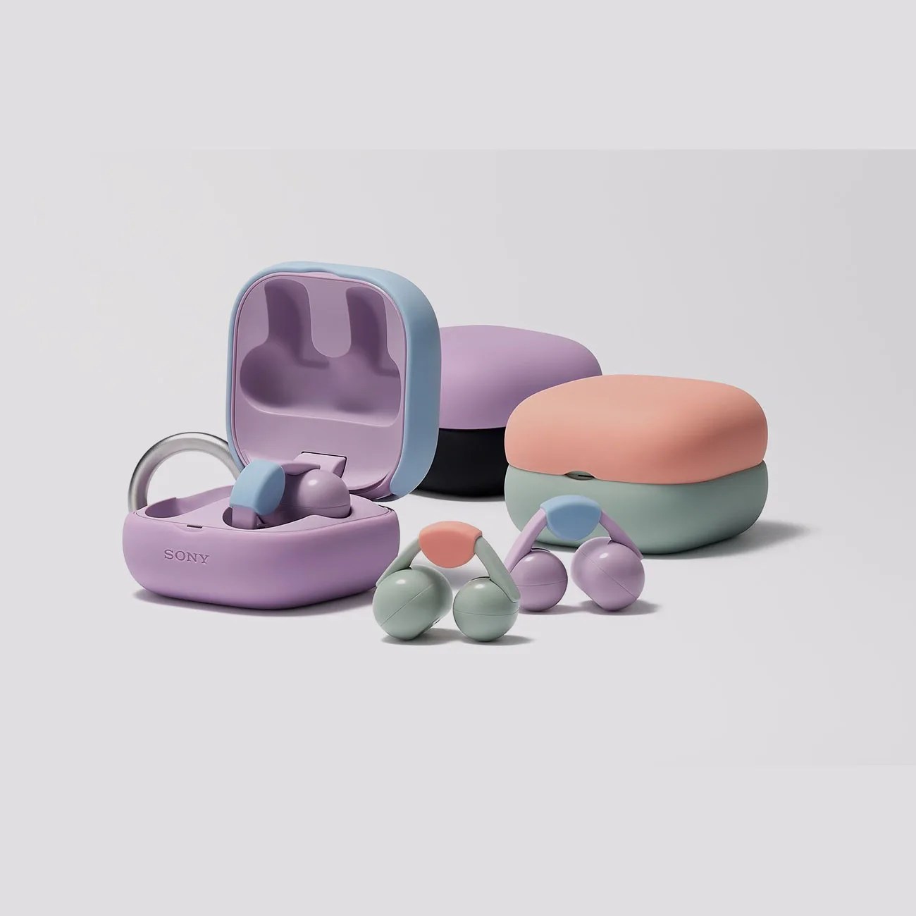 Three pairs of colorful Sony wireless earbuds with matching charging cases in pastel shades of purple, green, and peach on a light background.