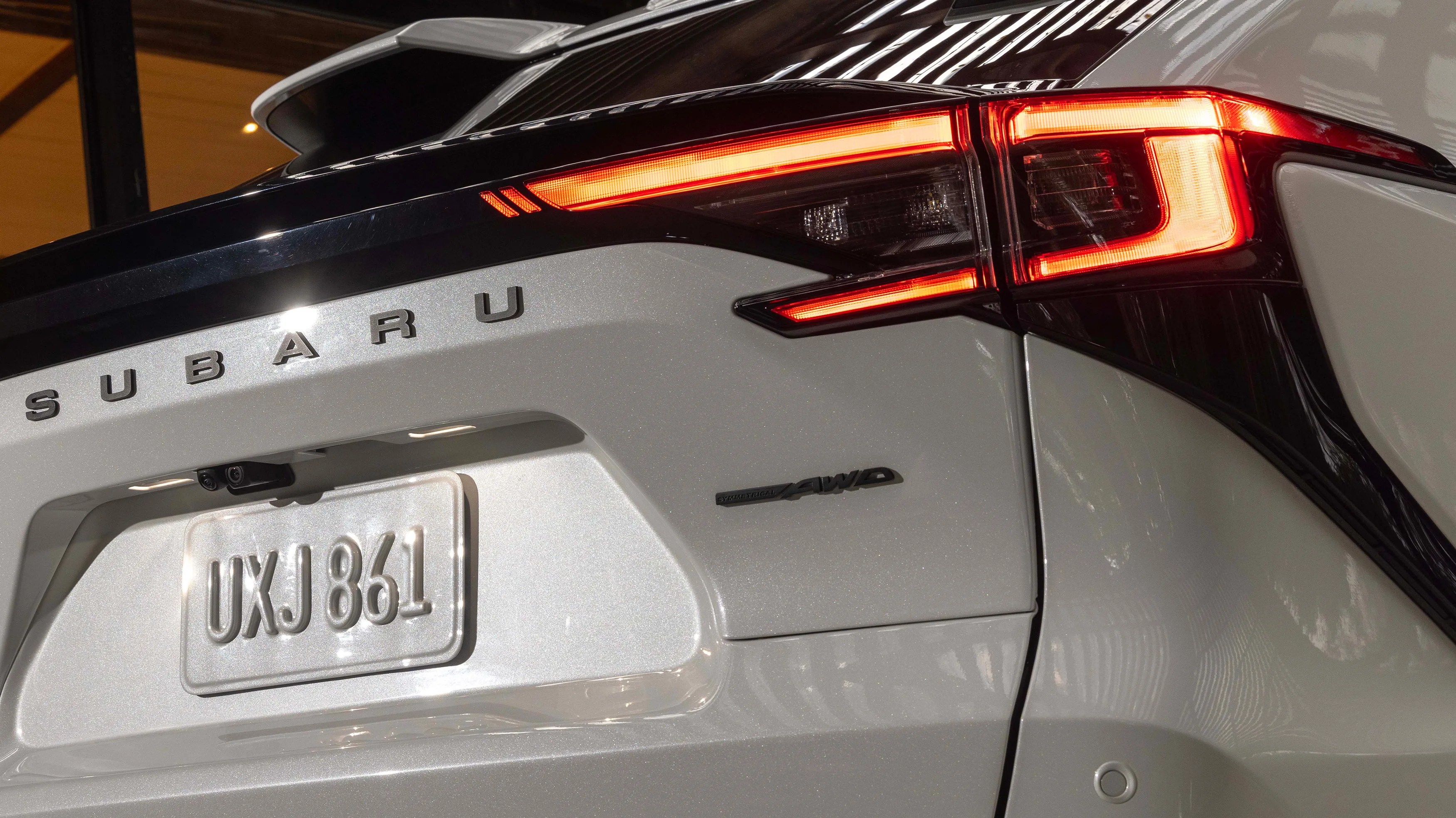 Rear view of a white Subaru car showing illuminated taillight, license plate UXJ 861, and AWD badge.