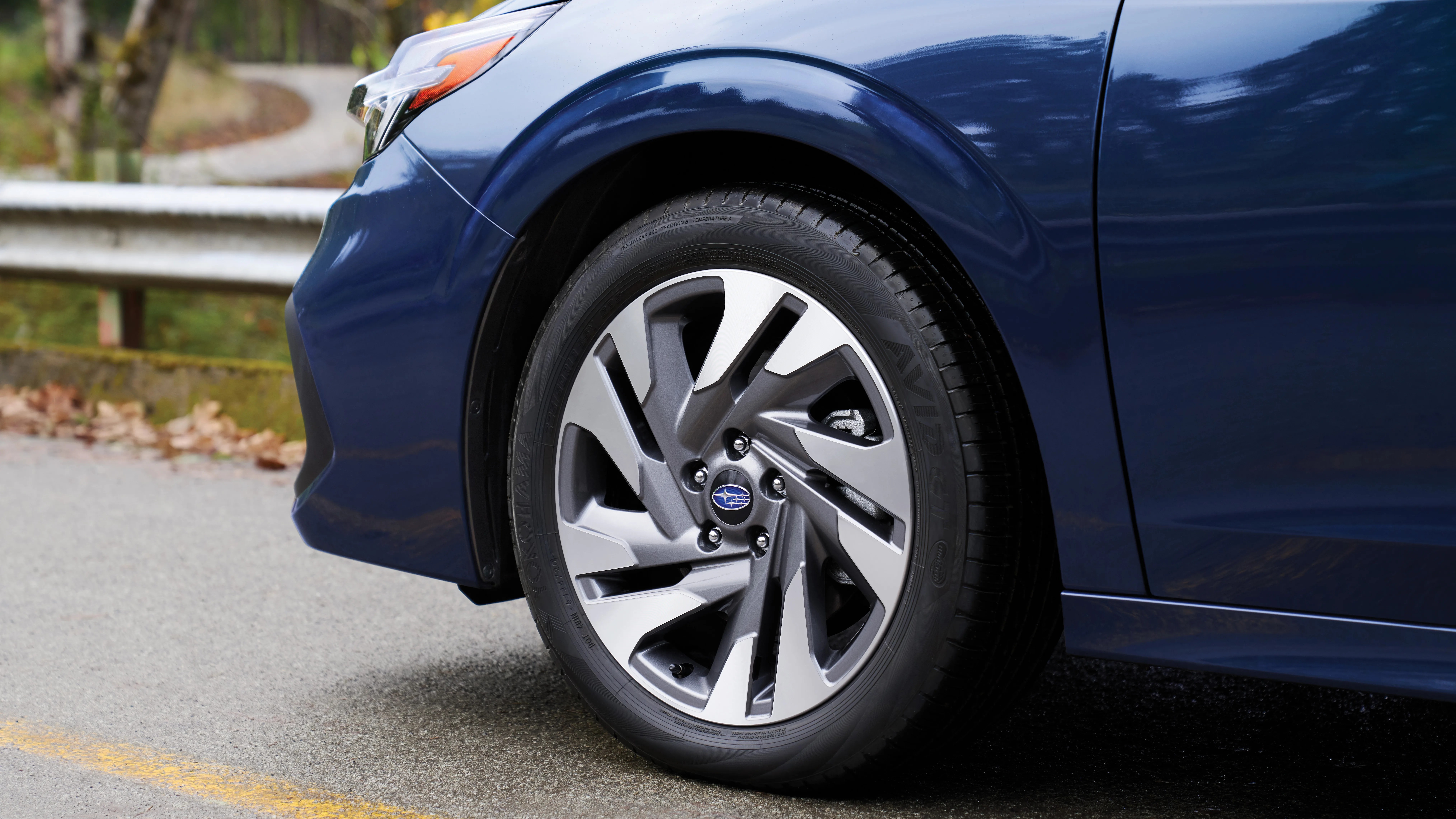 Close-up of a silver and gray Subaru alloy wheel on a dark blue car parked on a road.