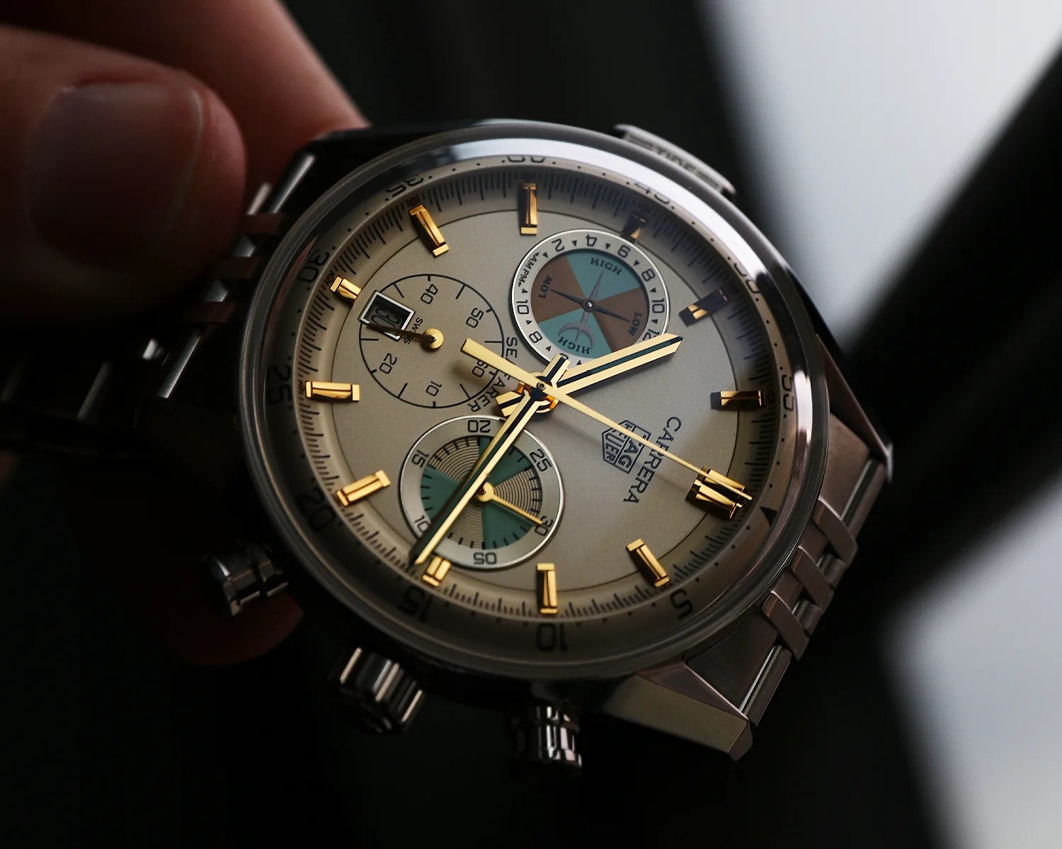Silver TAG Heuer Carrera watch with gold hour markers and hands, featuring three subdials and a metal bracelet.
