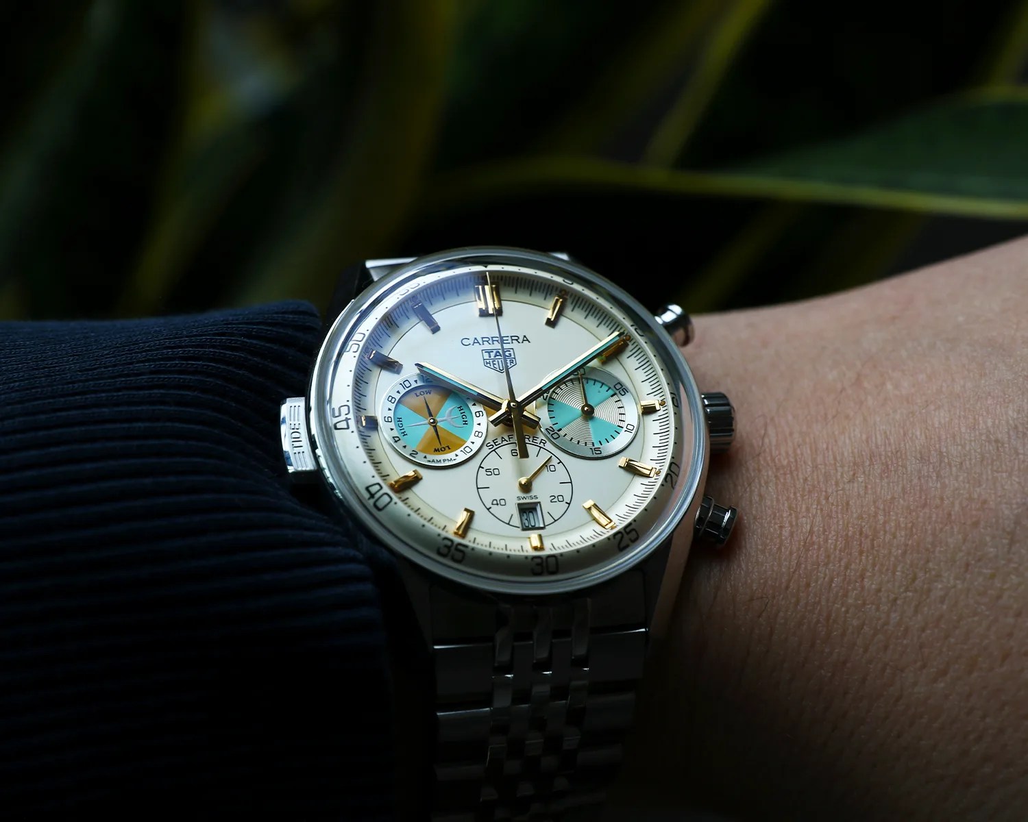 Silver TAG Heuer Carrera Seafarer wristwatch with white dial, gold hour markers, and blue subdials on a metal bracelet.