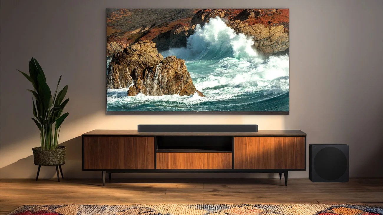 Flat-screen TV mounted on a wall above a wooden media console with a soundbar and subwoofer on a wooden floor.