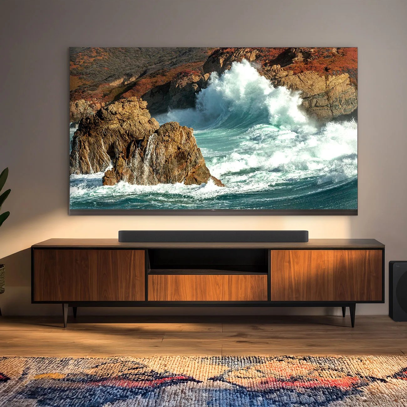 Wall-mounted flat-screen TV displaying ocean waves crashing against rocks above a wooden media console with a soundbar.