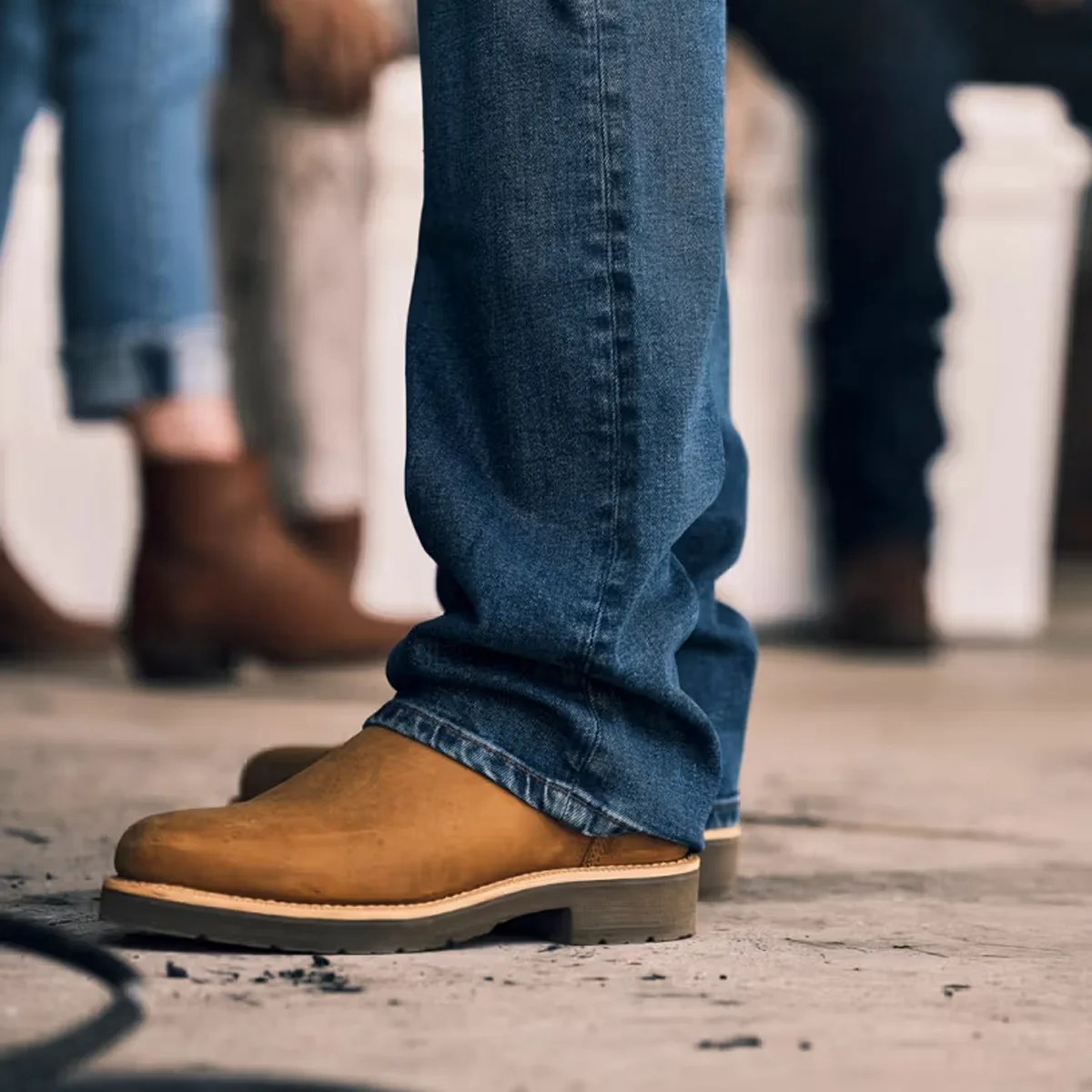 Tan leather boots worn with blue denim jeans on a concrete floor.