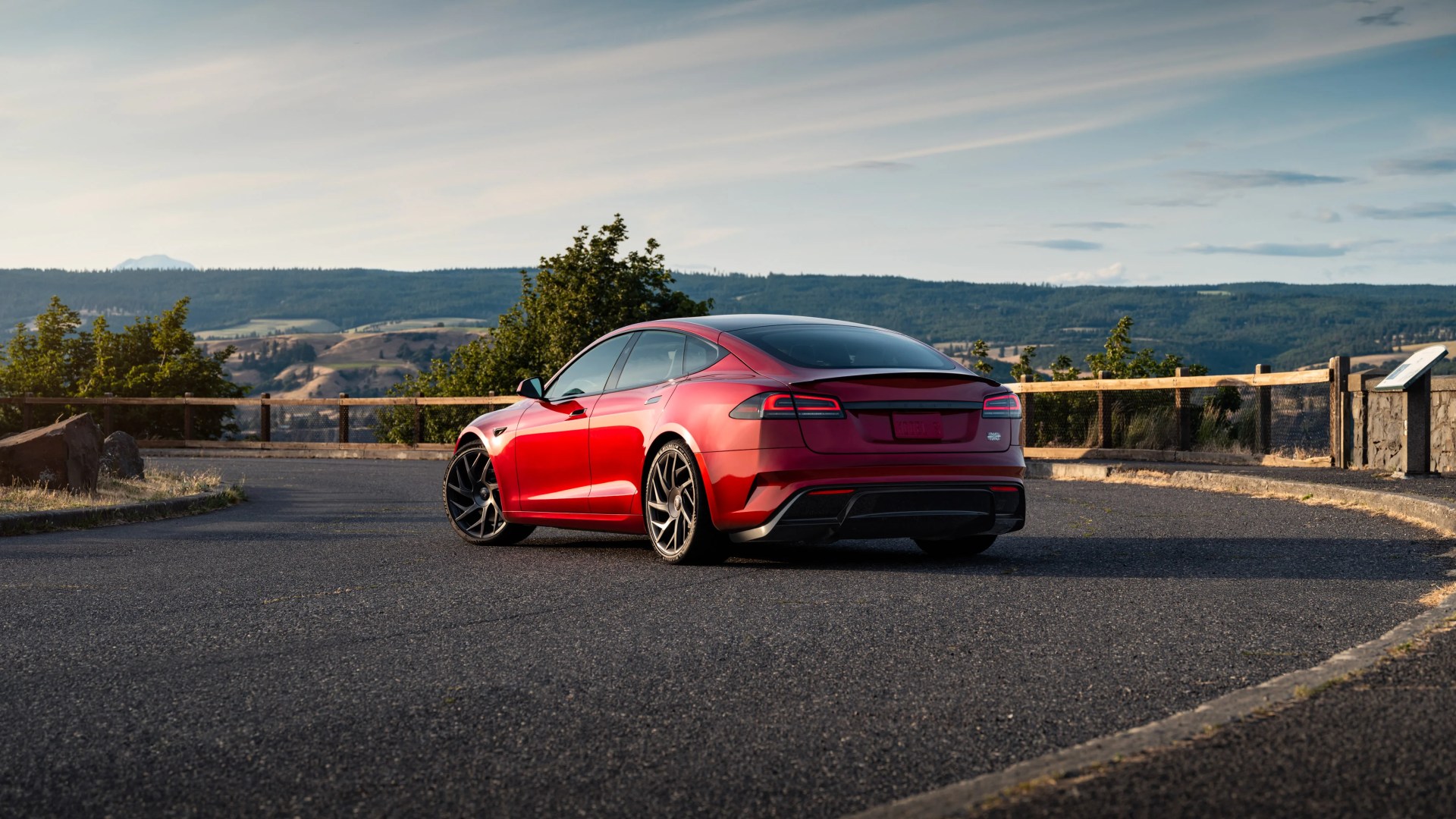 Red Tesla Model S parked on a curved asphalt road with mountains and trees in the background.