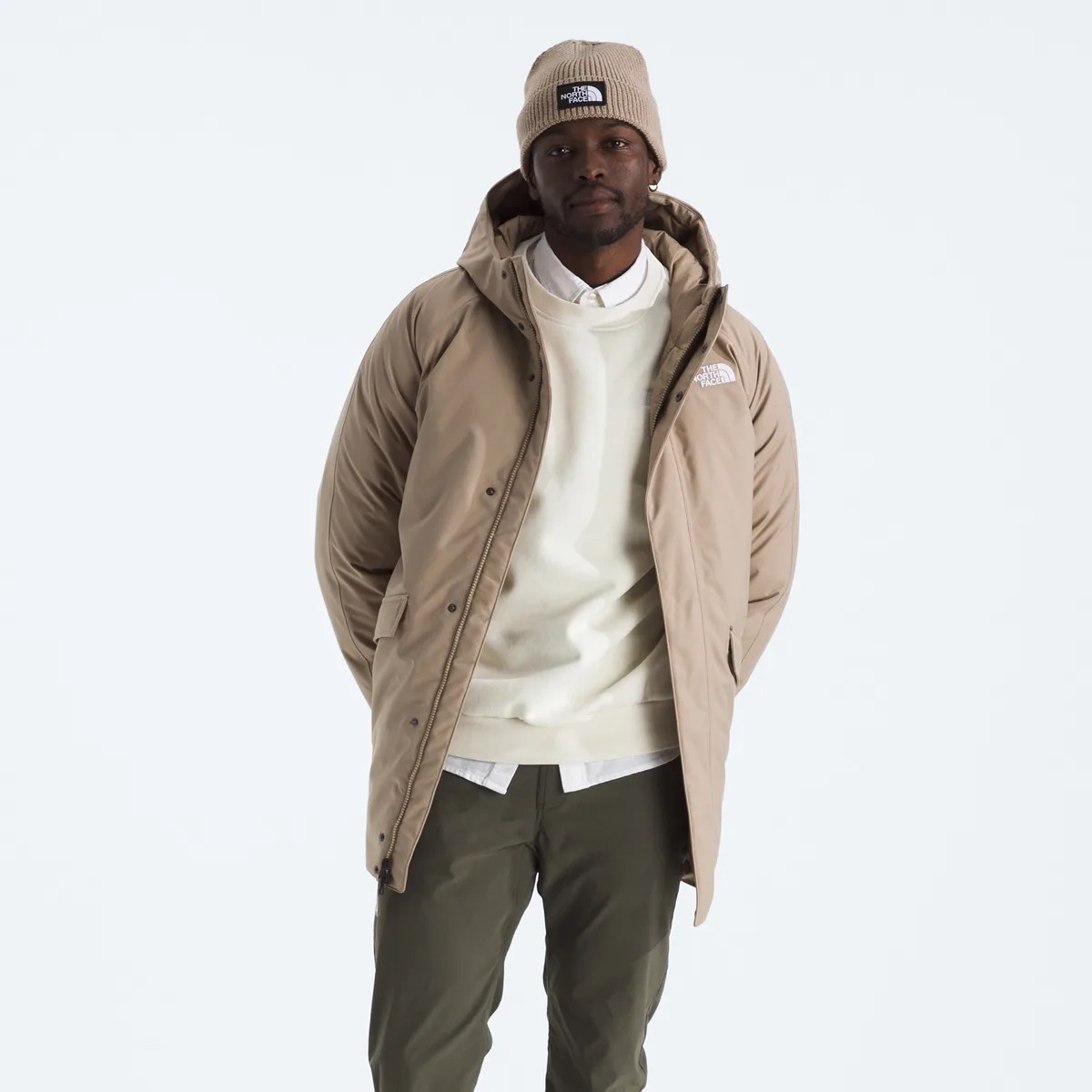 Man wearing a beige North Face parka, matching beanie, white sweatshirt, white shirt, and olive green pants.