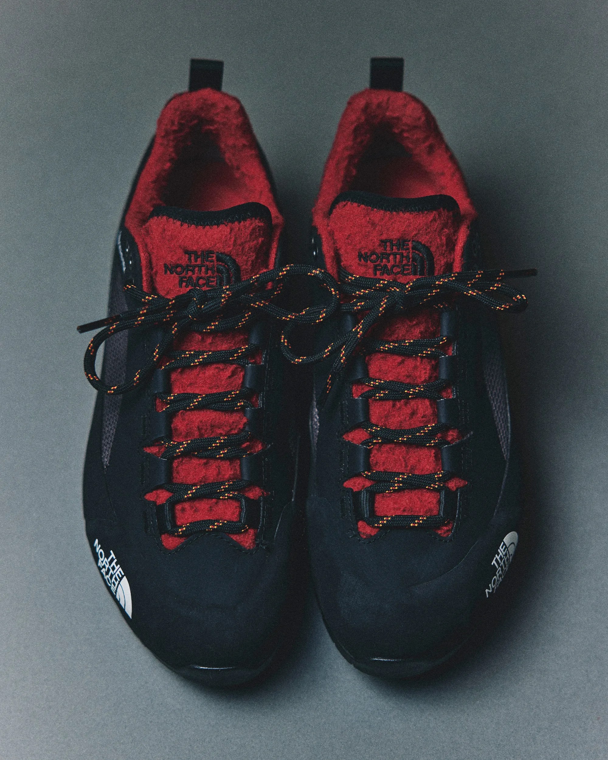 Pair of black and red The North Face sneakers with black and orange laces on a gray surface.