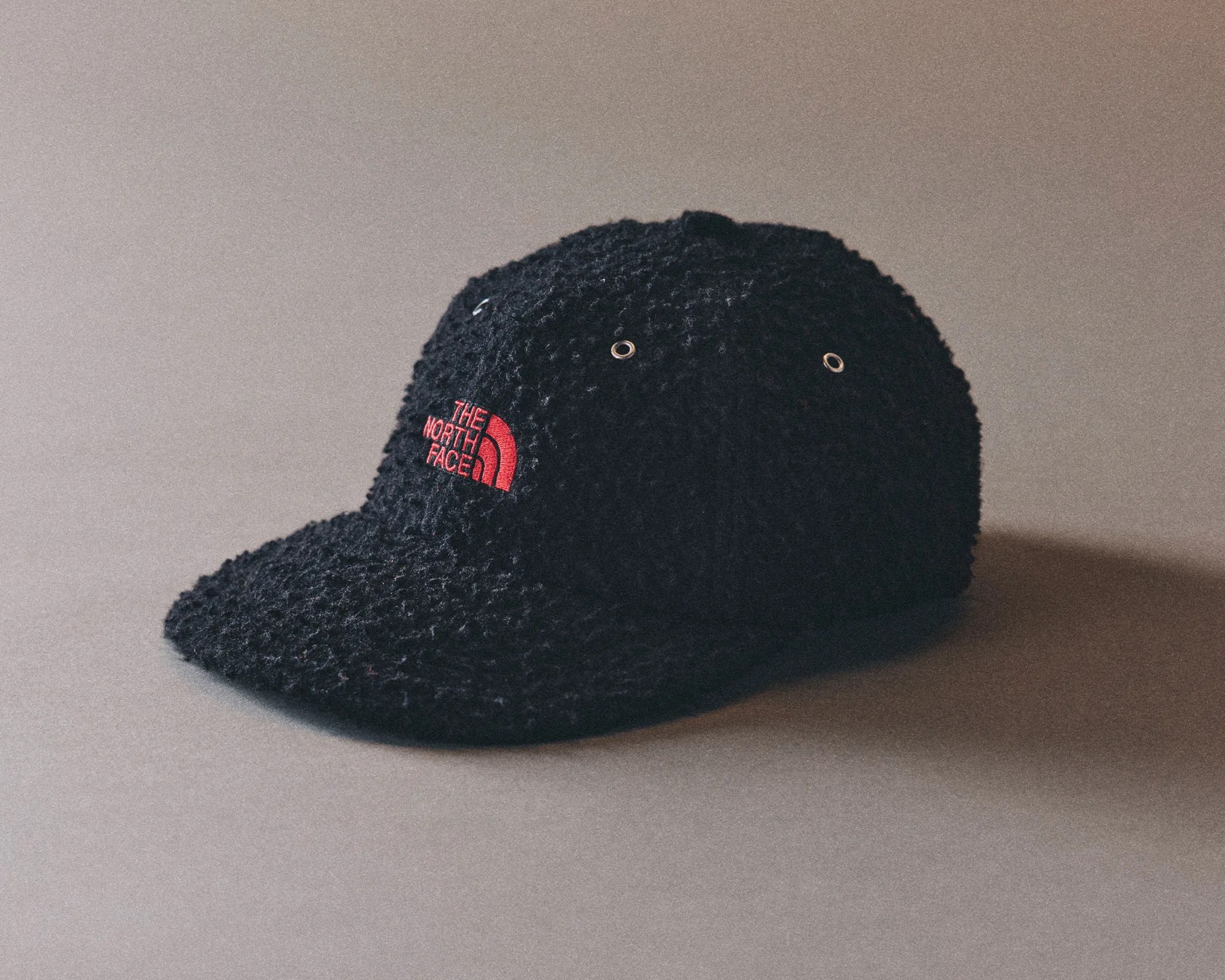 Black textured fleece baseball cap with red "The North Face" logo on front.