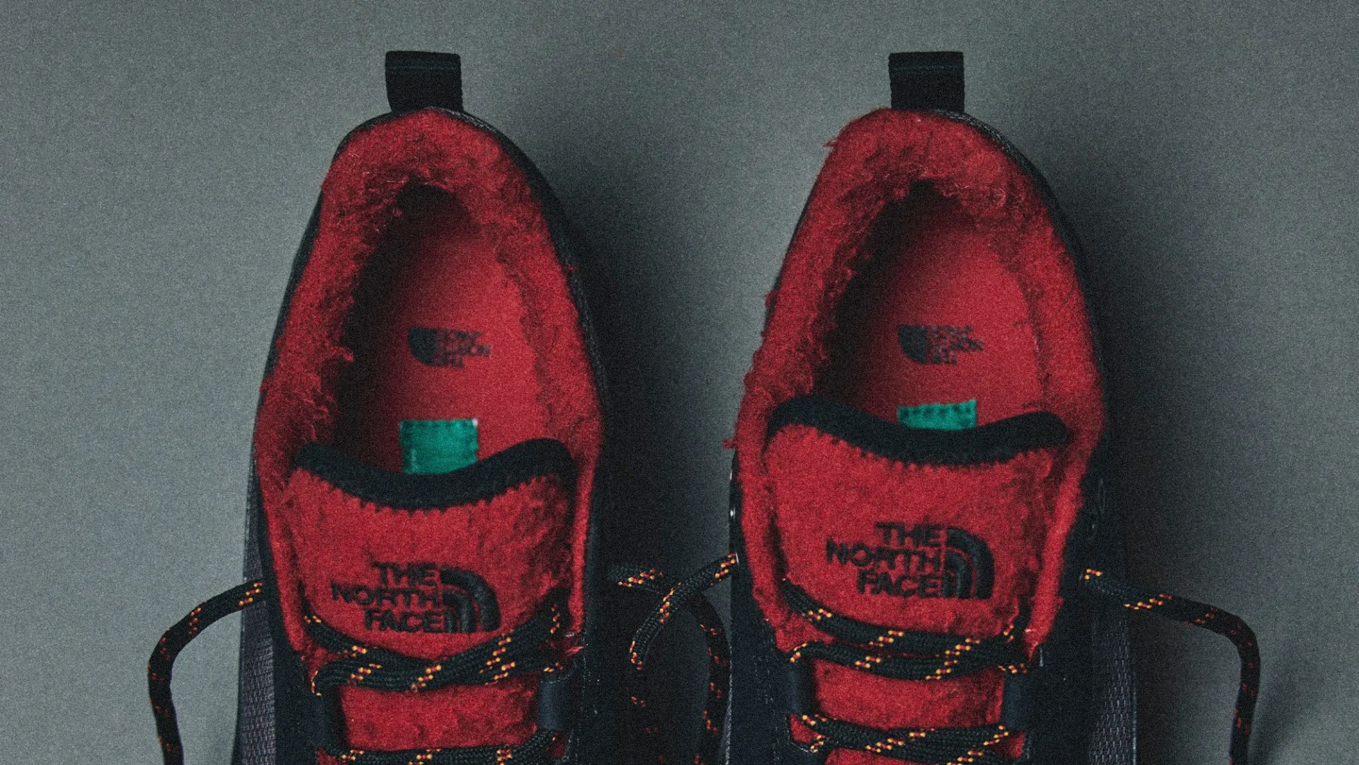 Pair of black and red The North Face shoes with fleece lining and patterned laces on a gray surface.