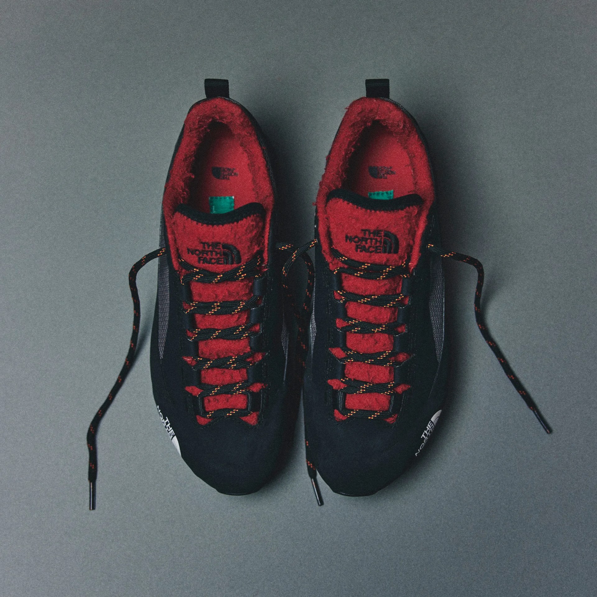 Pair of black and red The North Face sneakers with fleece lining and patterned laces on a gray surface.