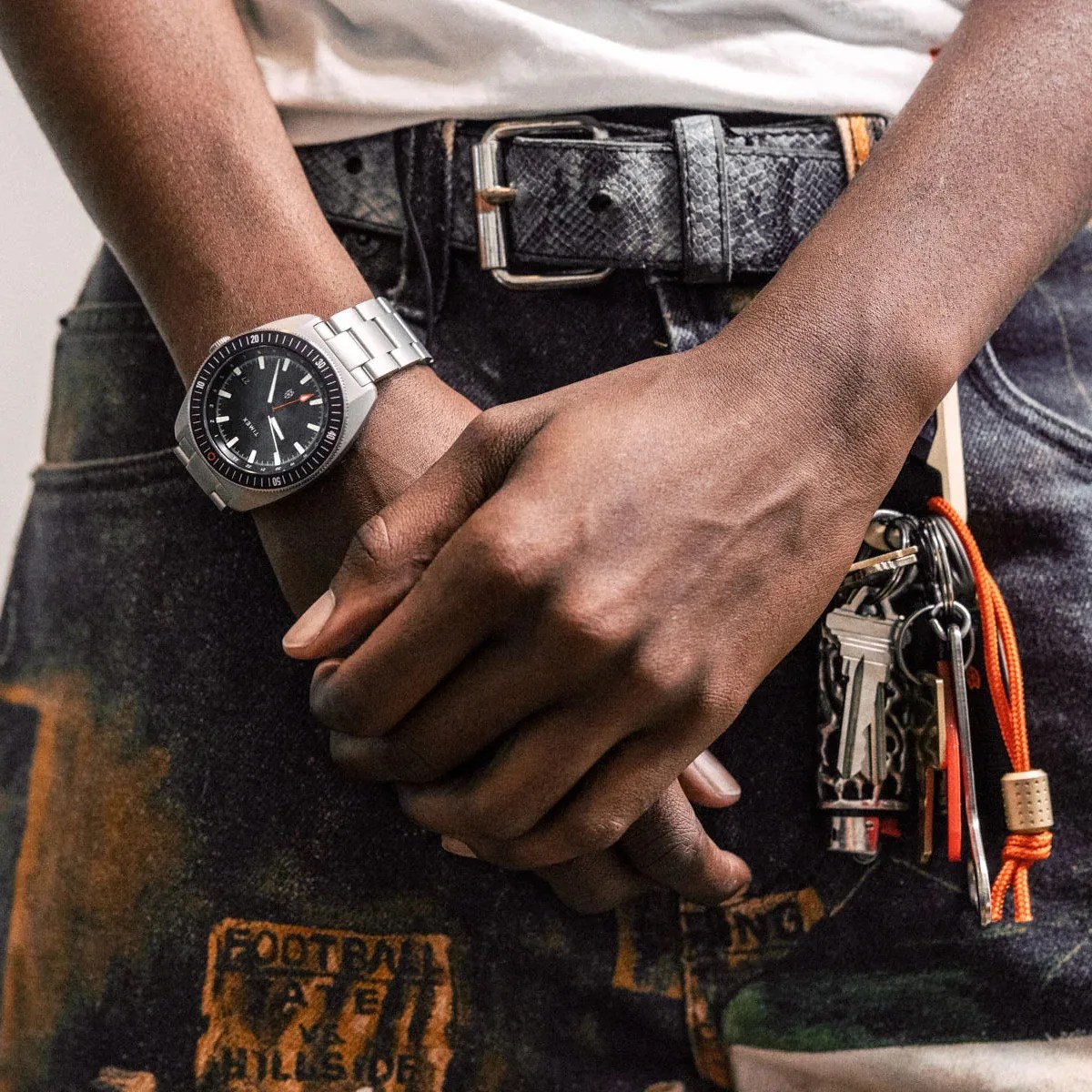 Close-up of hands clasped in front of a person wearing a silver metal wristwatch and holding a keychain with multiple keys and an orange lanyard.