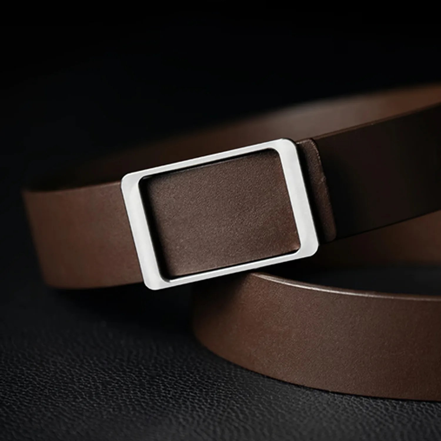 Brown leather belt with a rectangular silver buckle on a black textured surface.