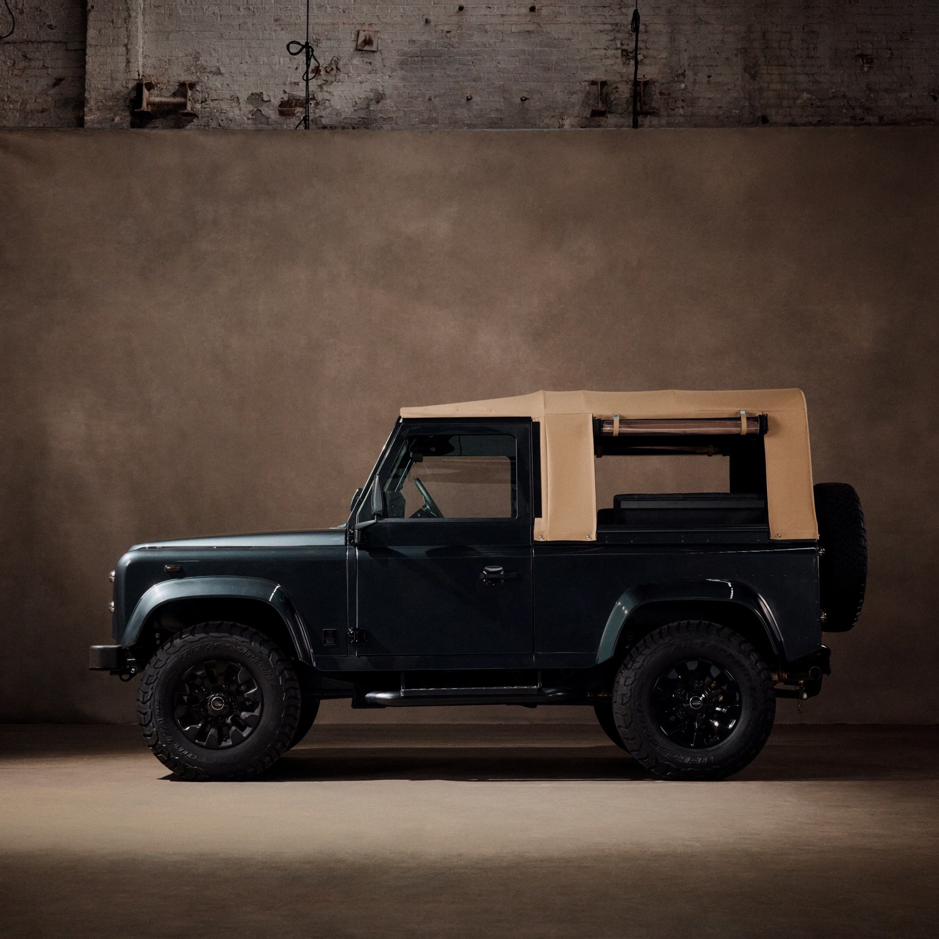 Dark green off-road vehicle with tan soft top and black wheels in a studio setting.
