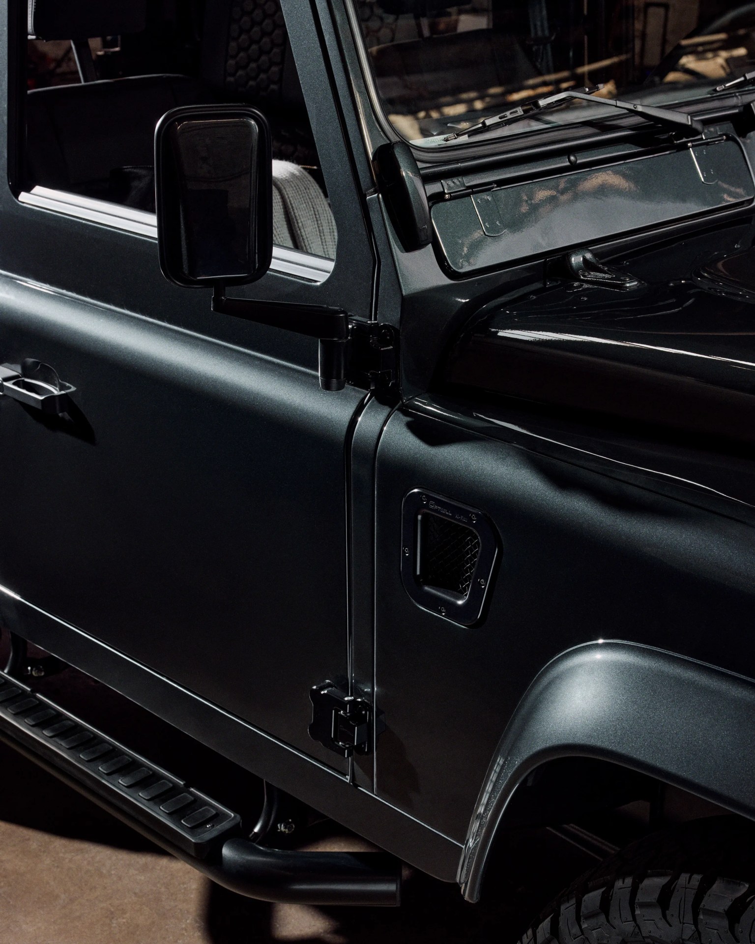 Close-up of a dark metallic gray off-road vehicle door and side mirror with rugged tire and step bar visible.