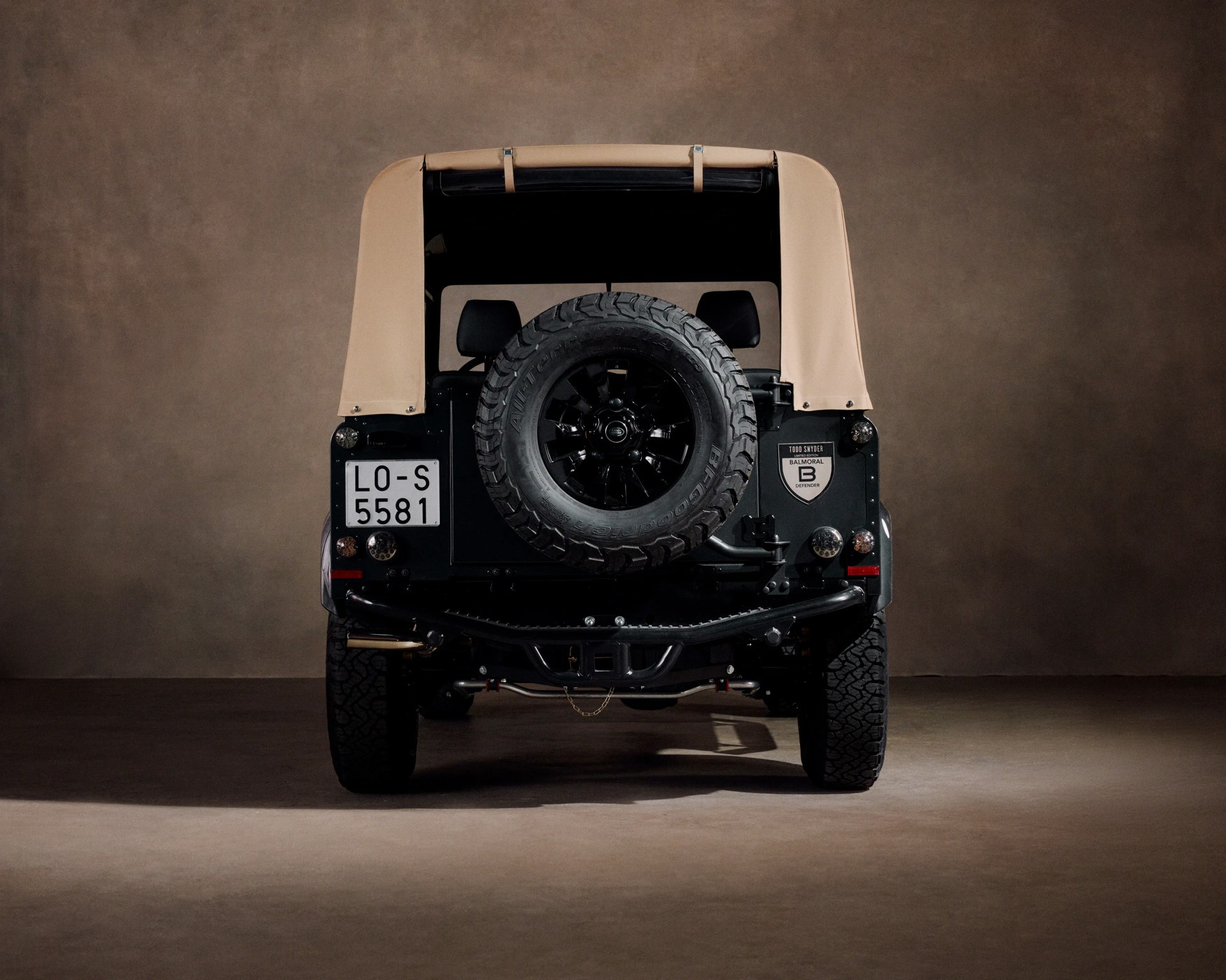 Rear view of a black off-road vehicle with a beige soft top and a spare tire mounted on the back.