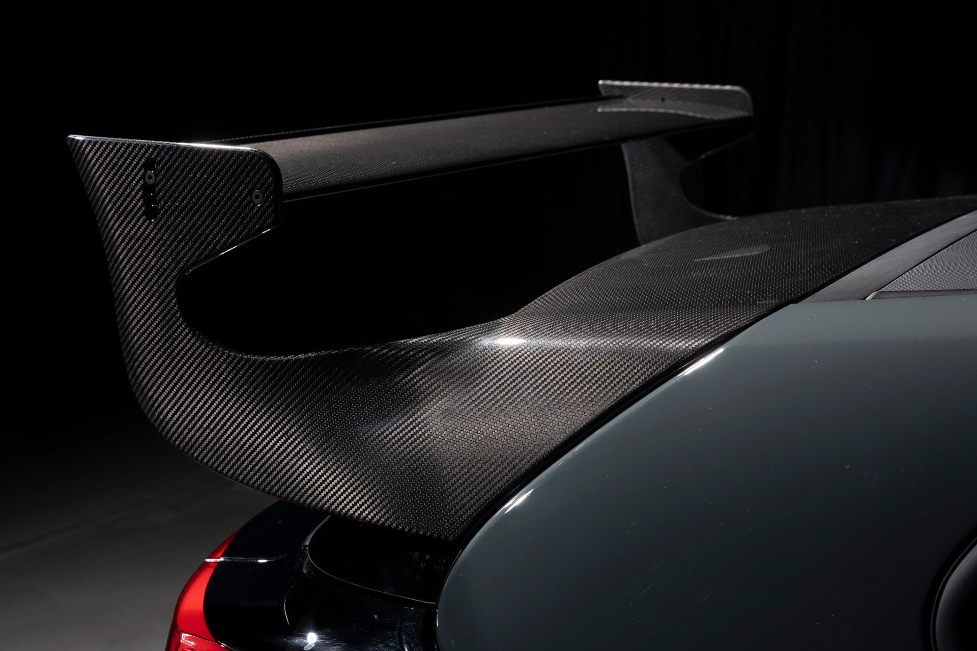 Glossy black carbon fiber rear spoiler mounted on a dark-colored sports car.
