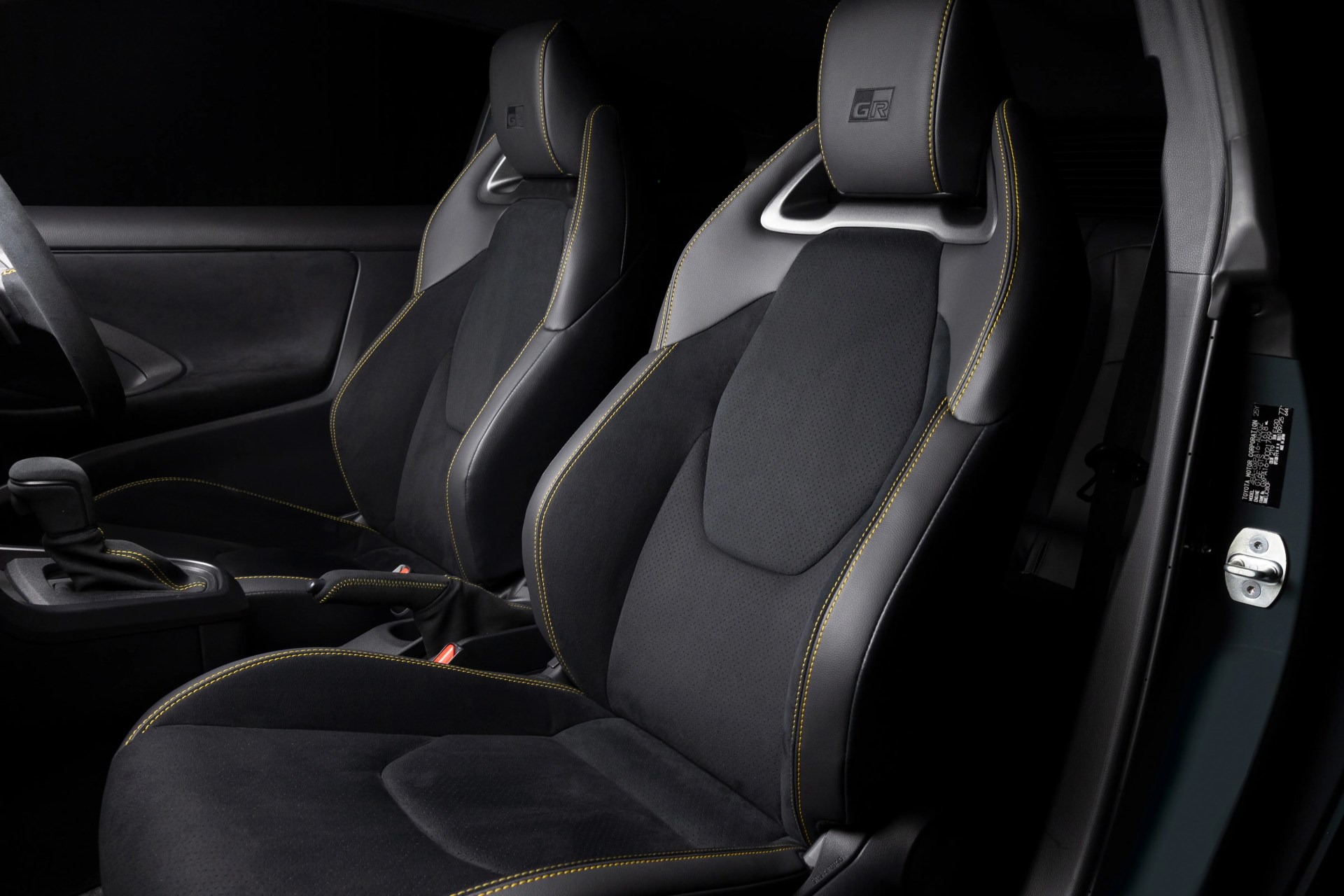 Two black leather and suede car seats with yellow stitching and GR logos on the headrests inside a vehicle.