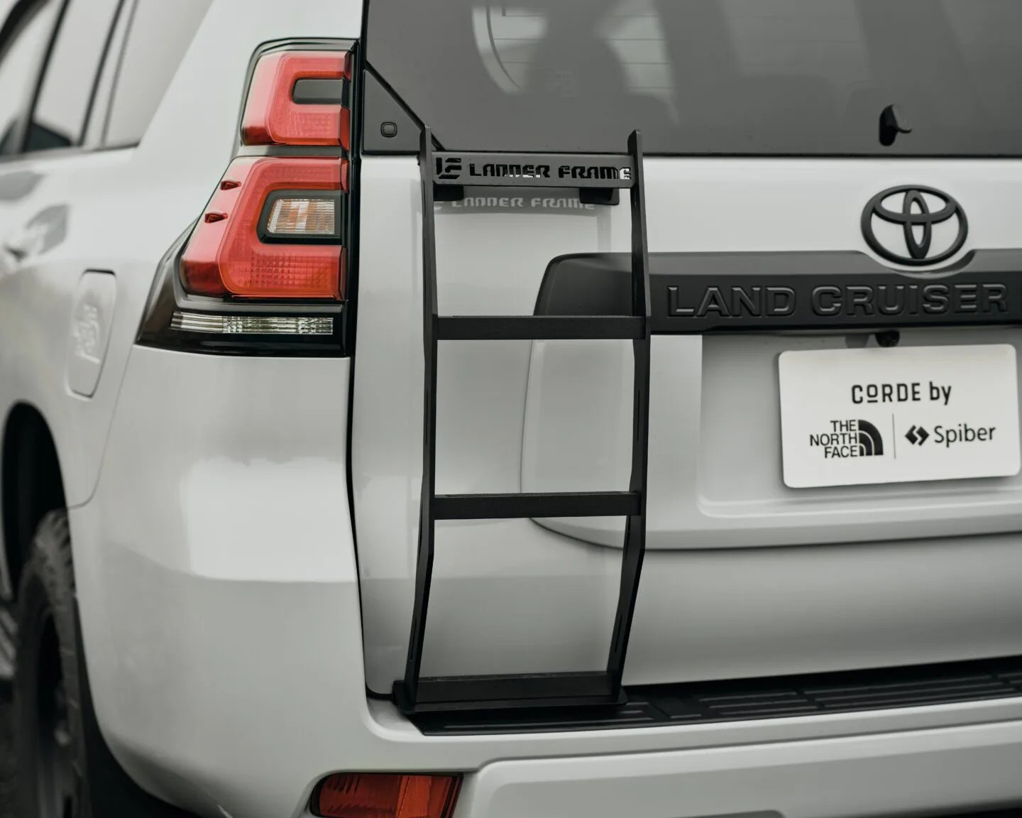 Black metal ladder frame attached to the rear door of a white Toyota Land Cruiser.