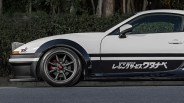 White and black sports car with Japanese racing service decal and dark alloy wheels on a street.