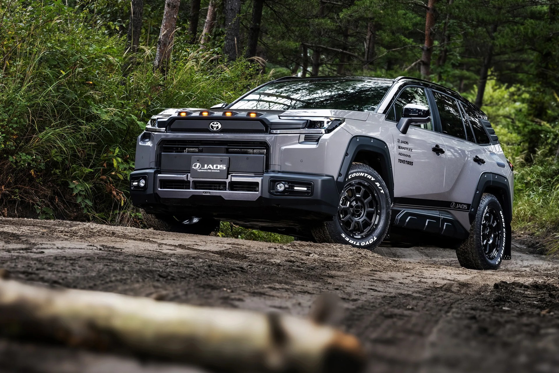 Gray Toyota SUV with black off-road modifications and Toyo tires on a dirt trail in a forest.
