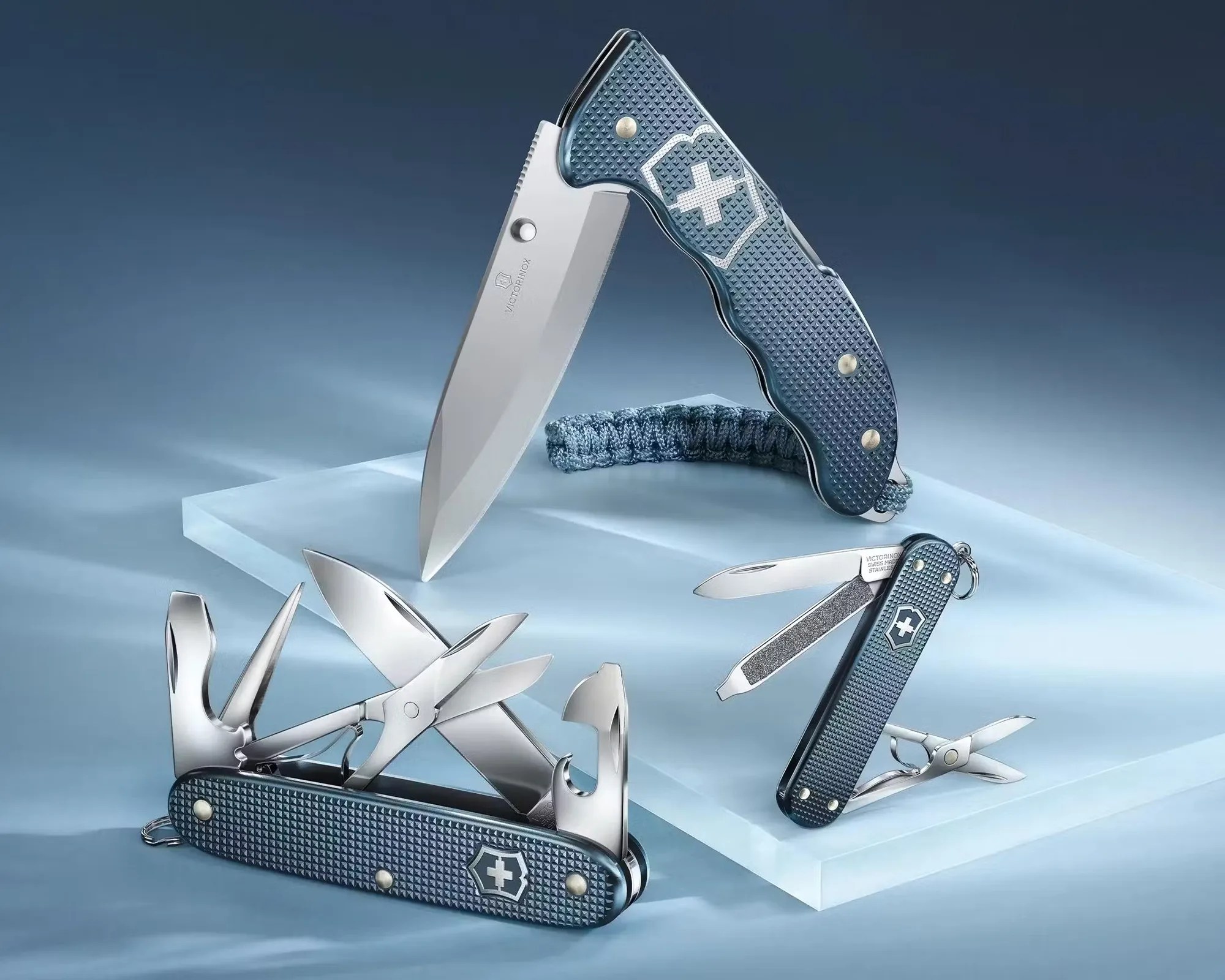 Three blue Victorinox Swiss Army knives with textured handles, each showing various open tools and blades on a light blue surface.