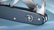 Blue textured Swiss Army knife with partially opened tools on a light blue surface.