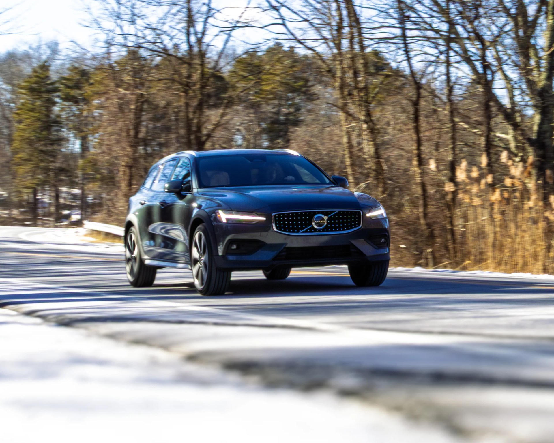 Dark blue Volvo SUV driving on a snow-lined road with leafless trees in the background.