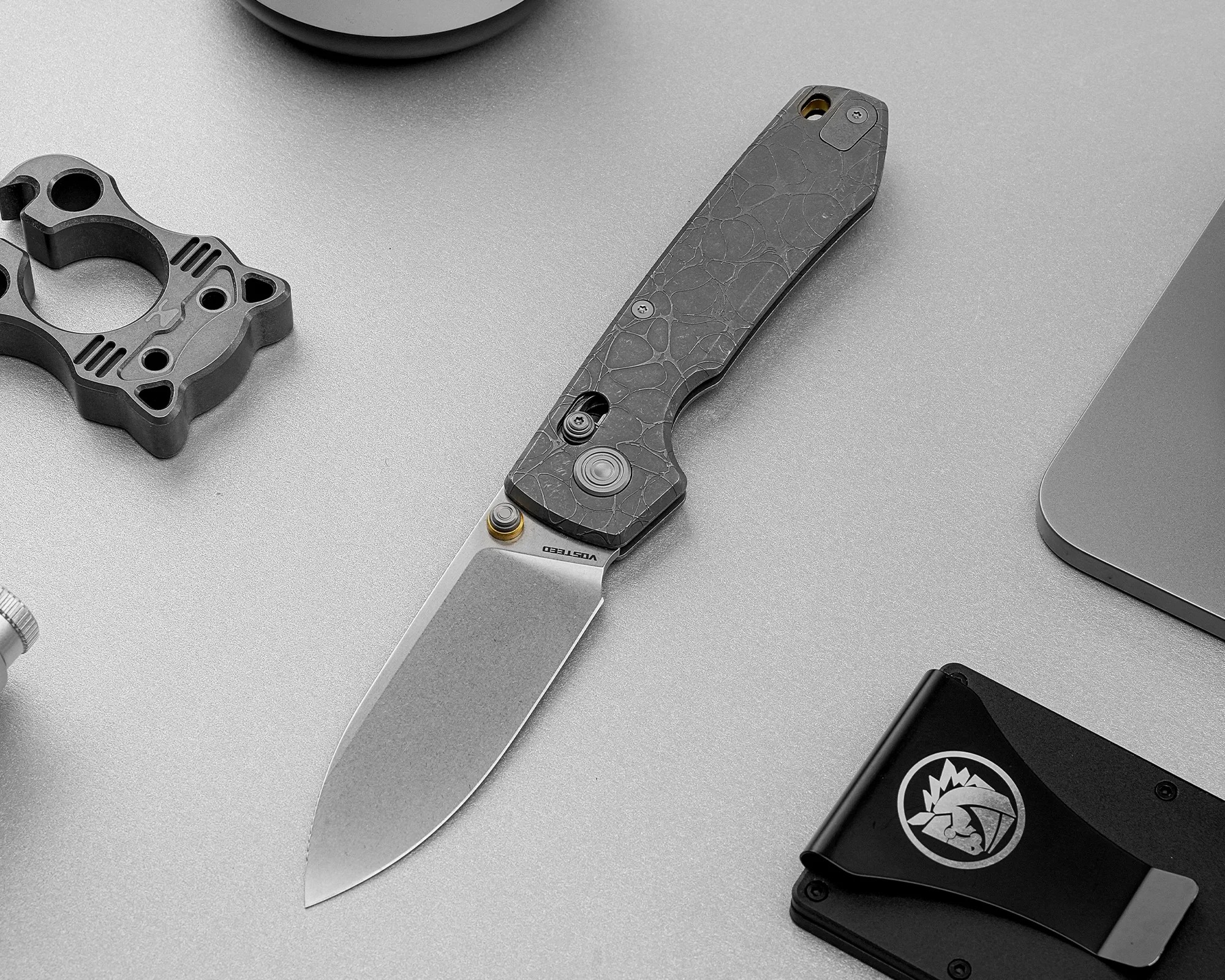 Folding knife with a stonewashed blade and textured dark handle on a gray surface.