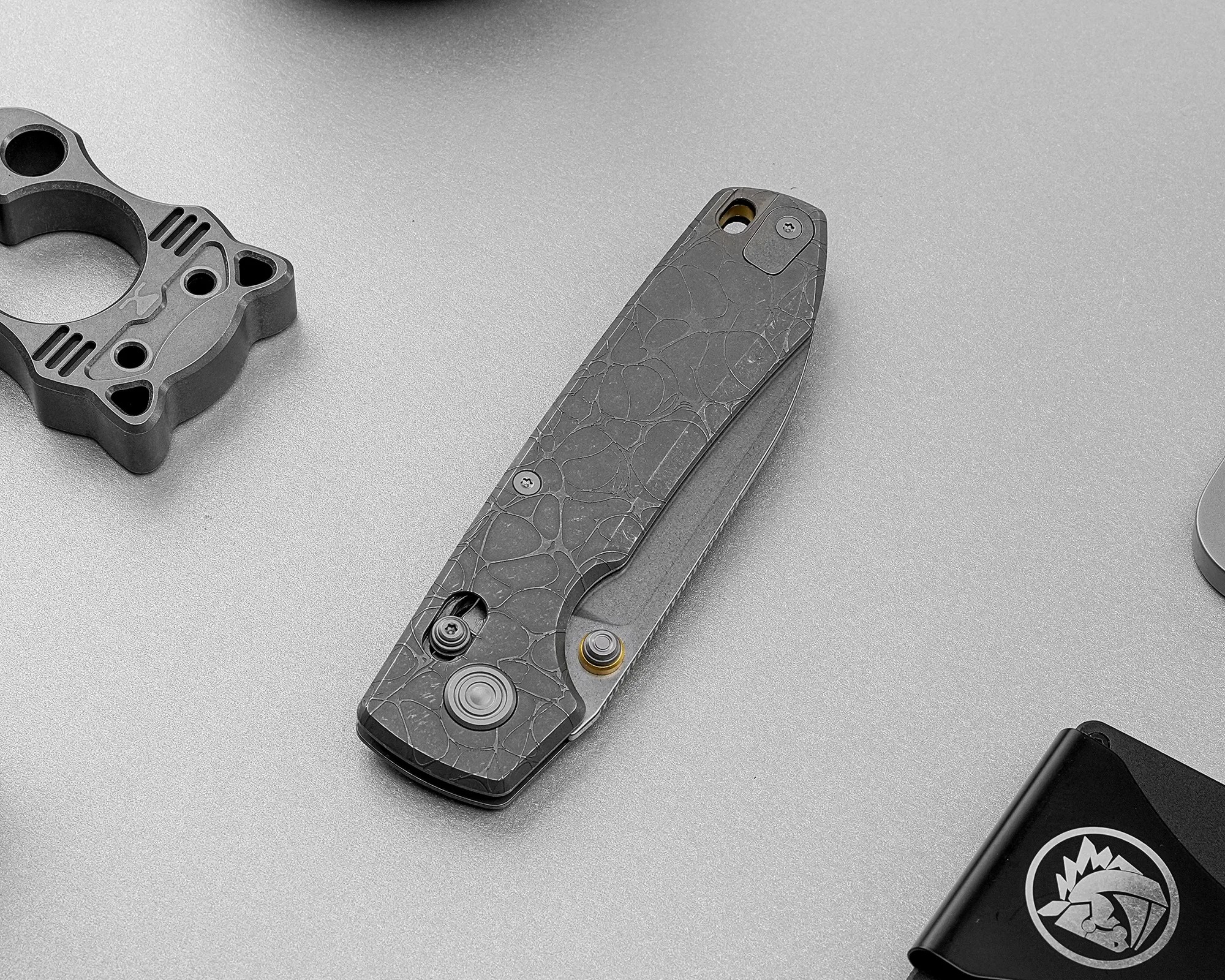 Closed folding knife with a textured dark handle and visible screws on a gray surface.
