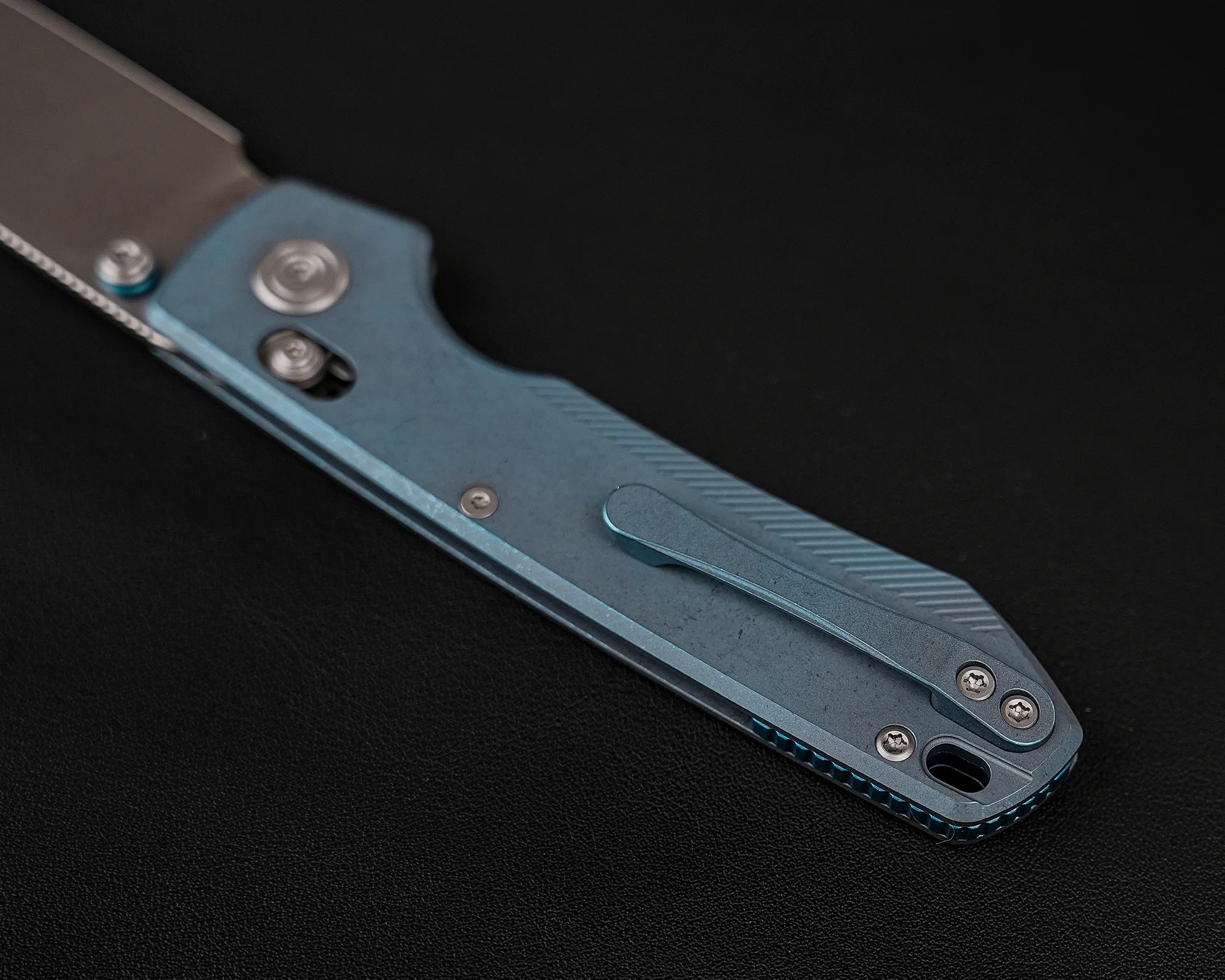 Blue titanium folding knife handle with pocket clip and screws on a black surface.