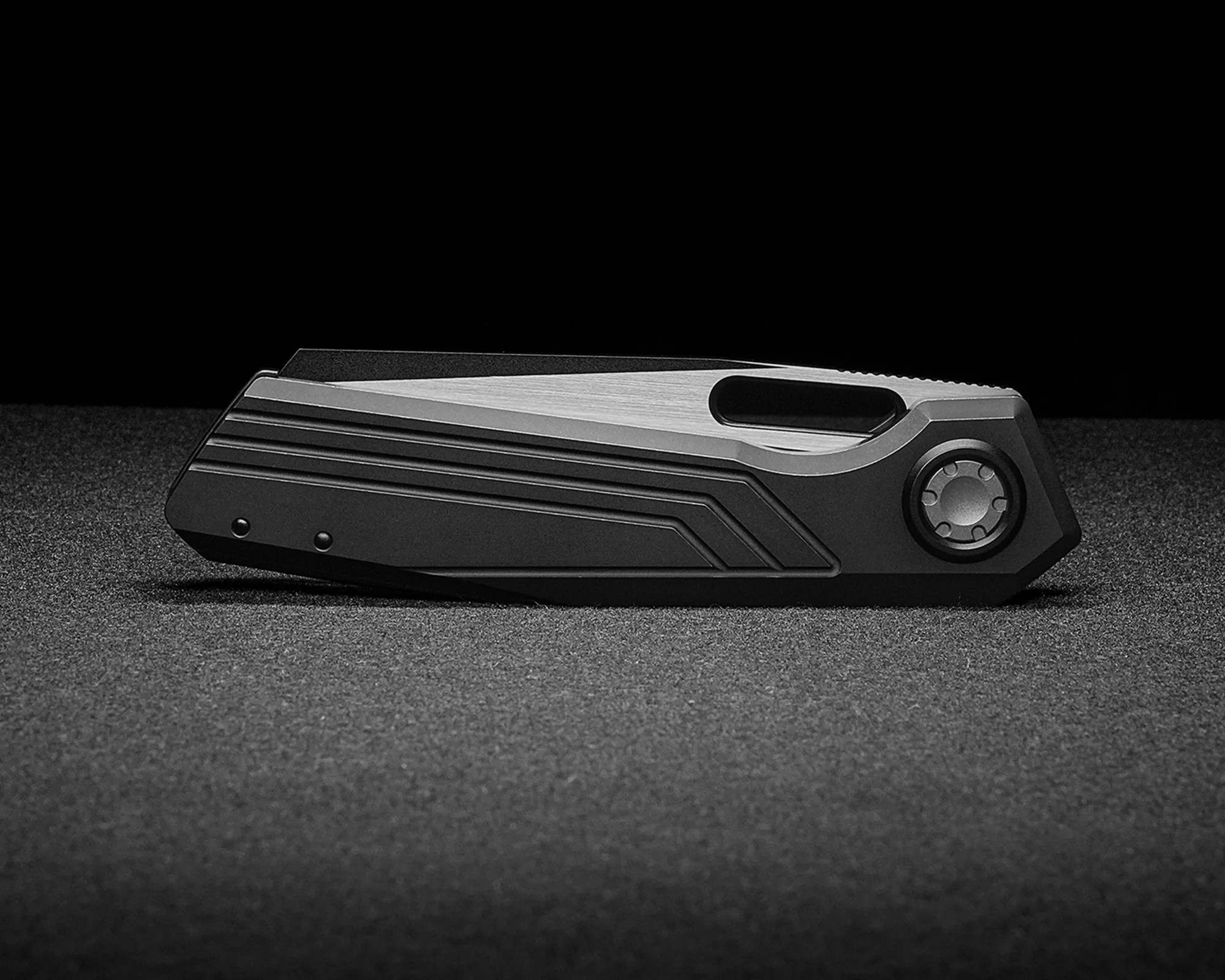 Closed black and silver folding knife with textured grip on a dark surface.