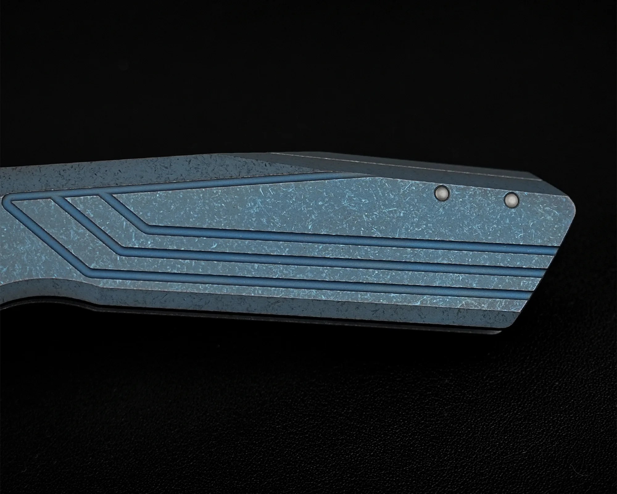 Close-up of a blue-gray textured metal object with parallel grooves and two small round rivets on a black background.